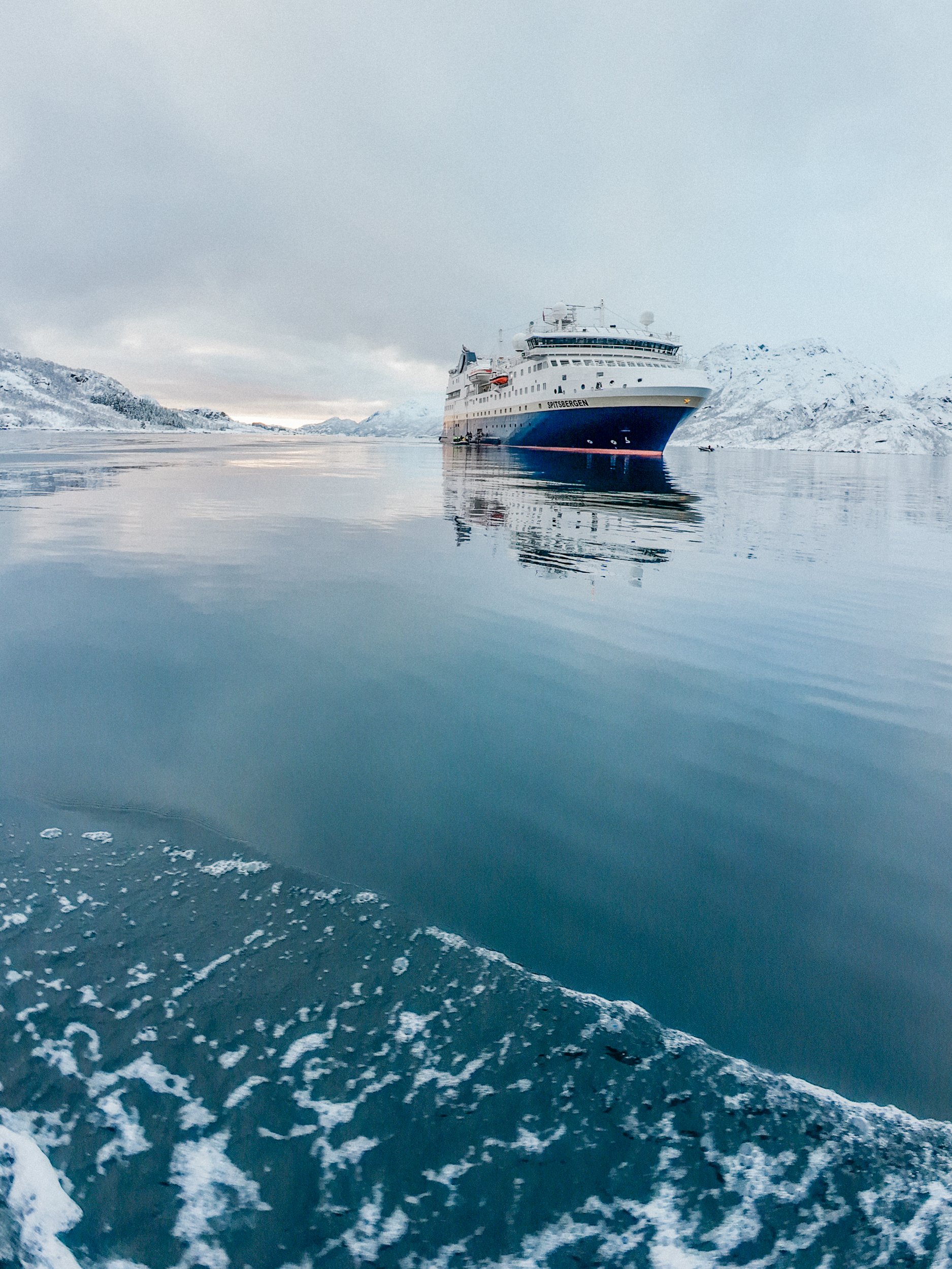 An HX Expeditions ship sailing in icy waters in Norway with snow-covered mountains in the background.