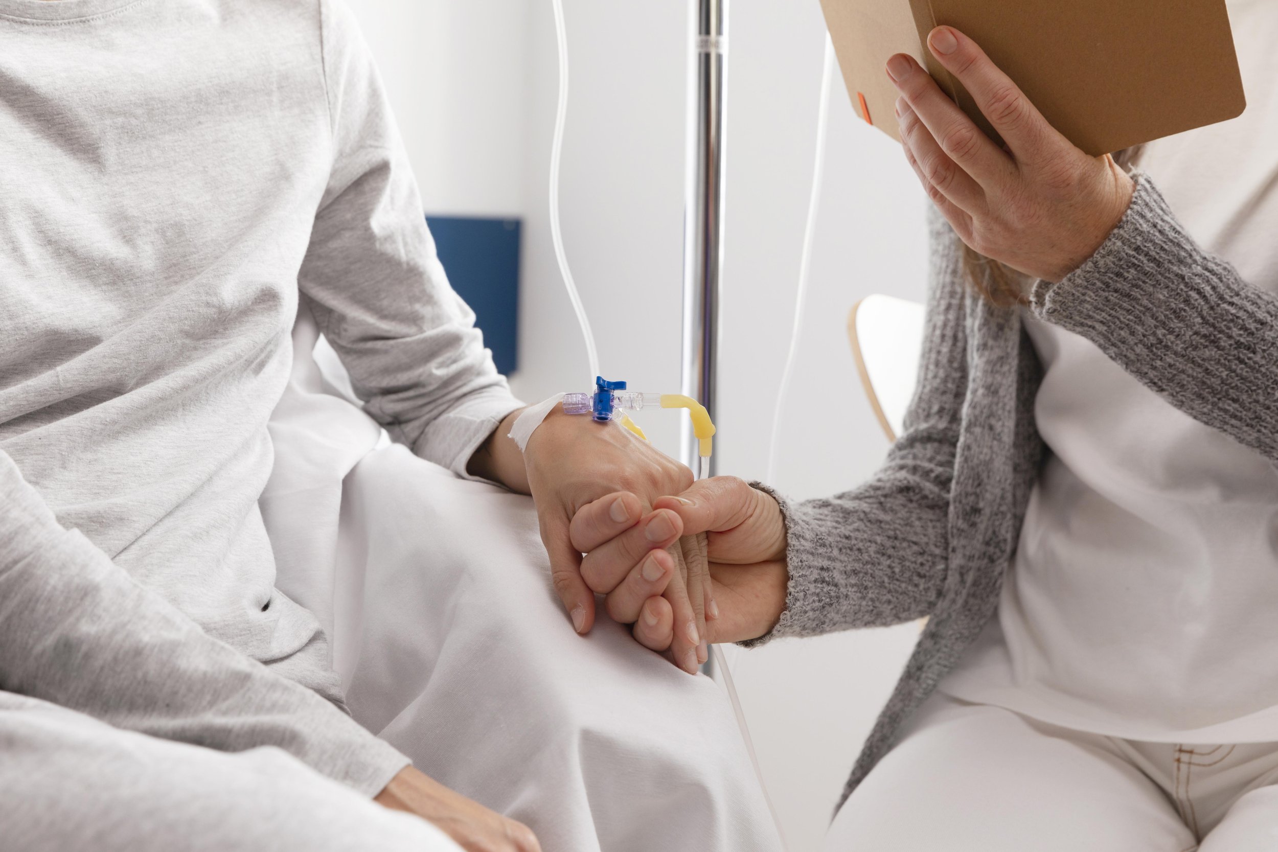 Person in a hospital bed with an IV line, holding hands with another person.