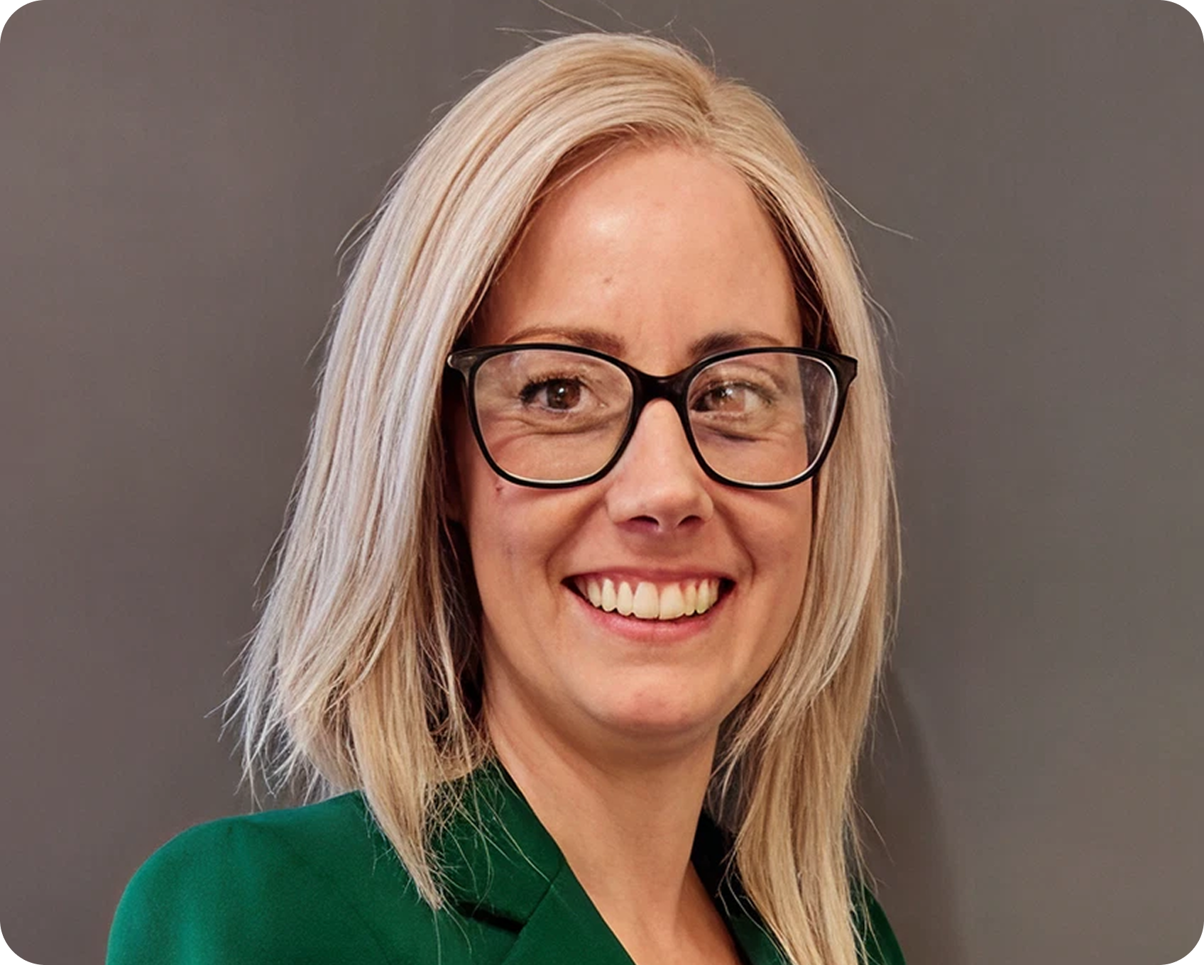 A woman with blonde hair, glasses, and a green top smiling against a gray background.