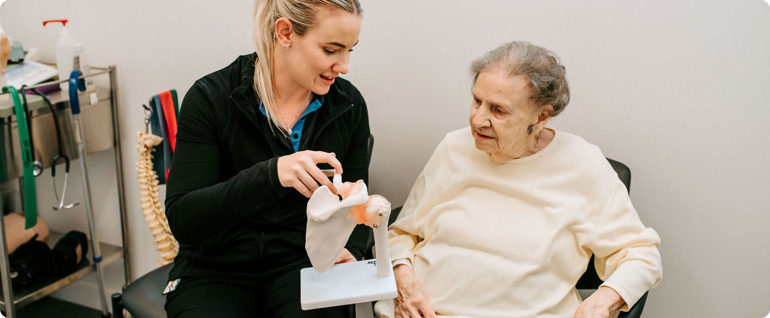 A healthcare worker shows a model of a hip joint to an elderly woman in a medical office.