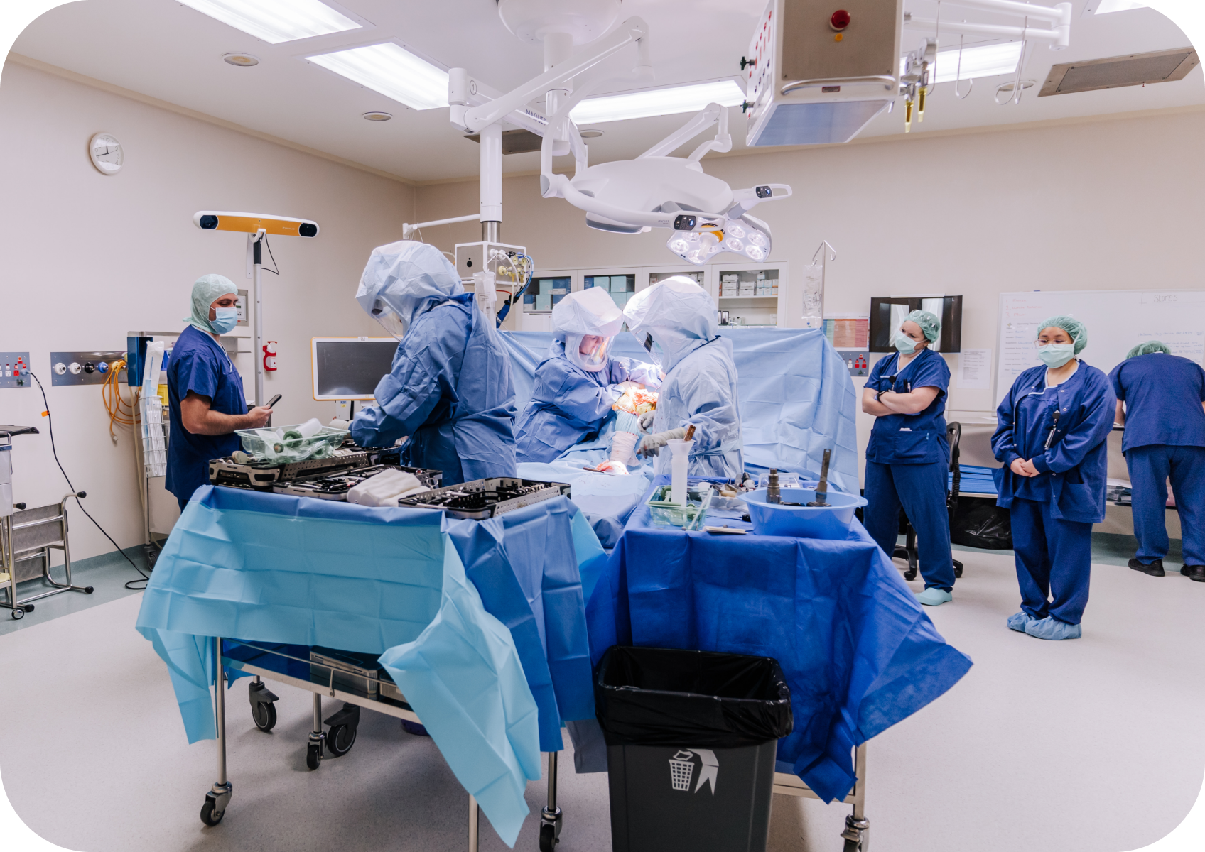 Medical team performing surgery in an operating room, with equipment and monitors around them.