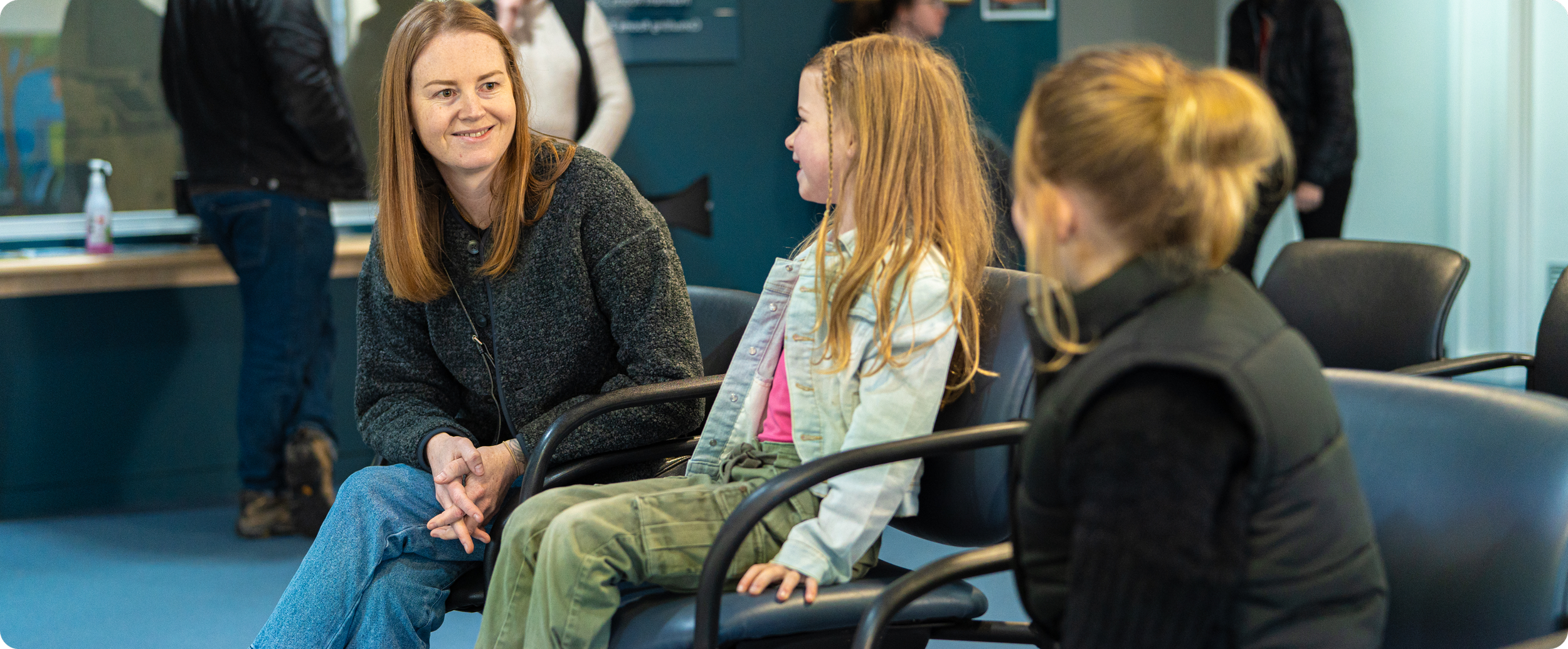 A woman and a young girl are sitting and talking in an airport waiting area, engaging in a pleasant conversation.