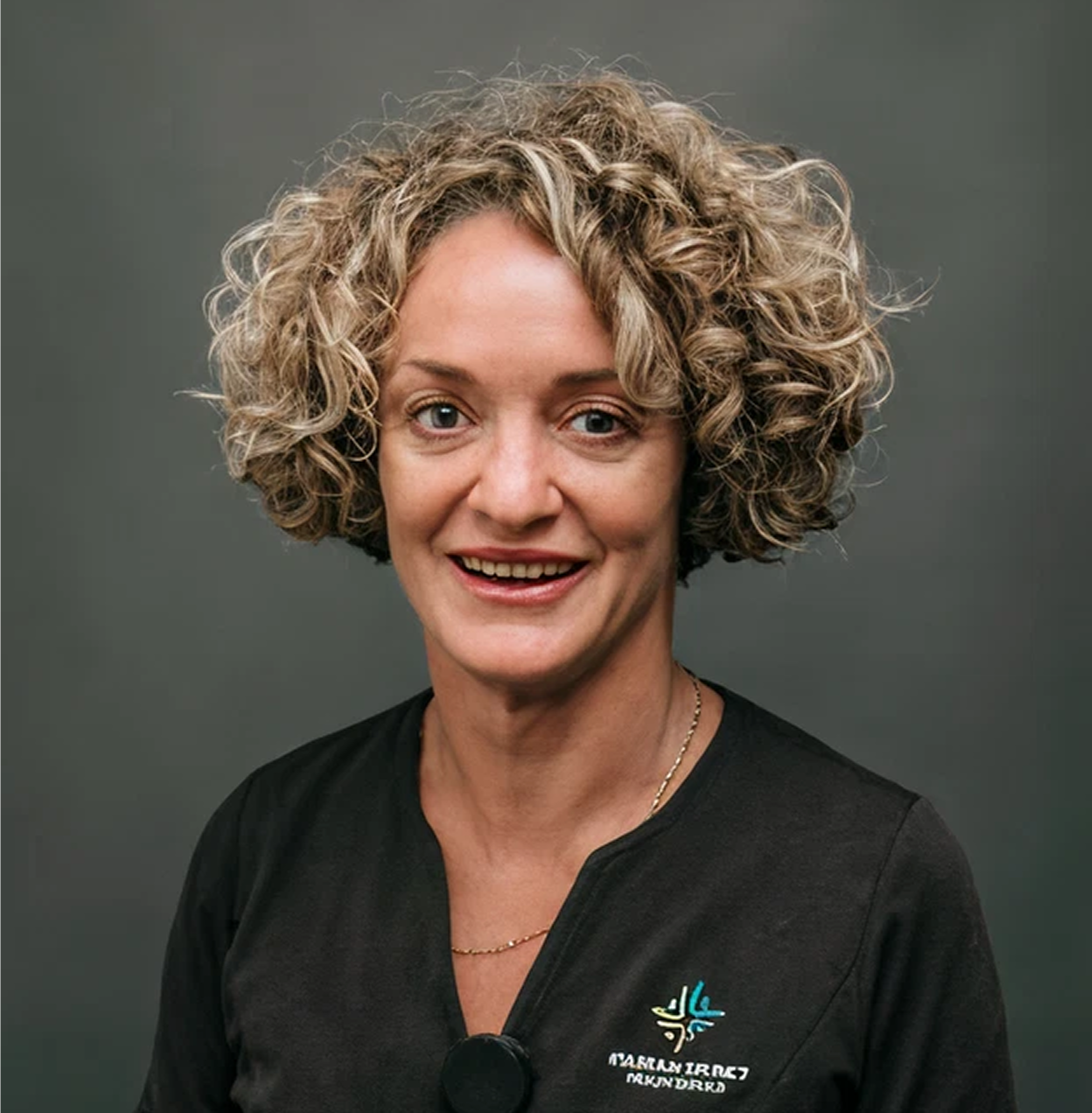 Headshot of a woman with curly blonde hair, smiling, wearing a black shirt with a logo.