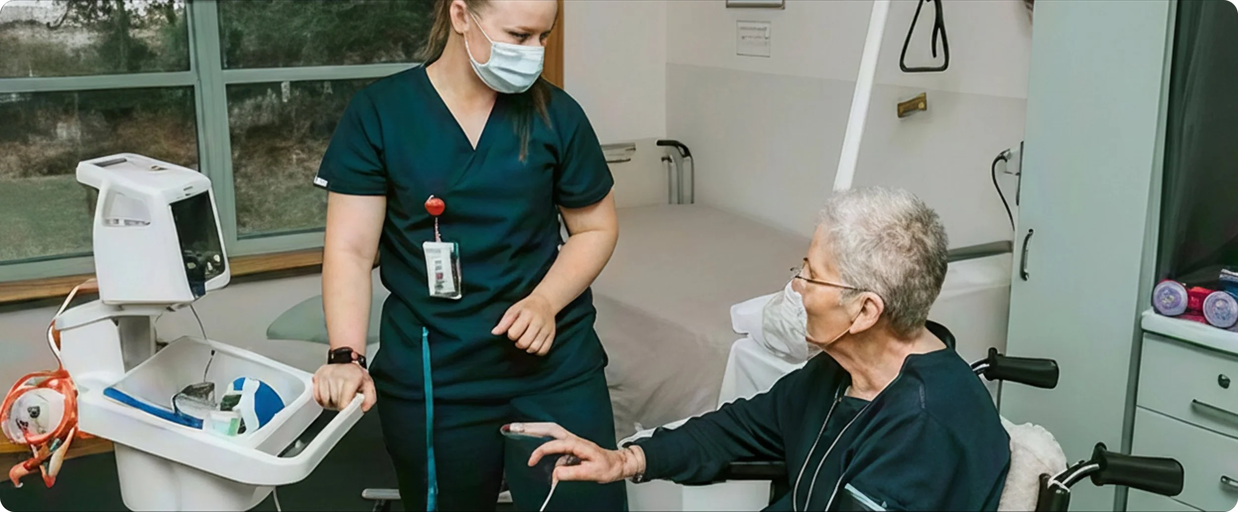 A healthcare worker and an elderly patient wearing face masks in a medical setting, with medical equipment around them.