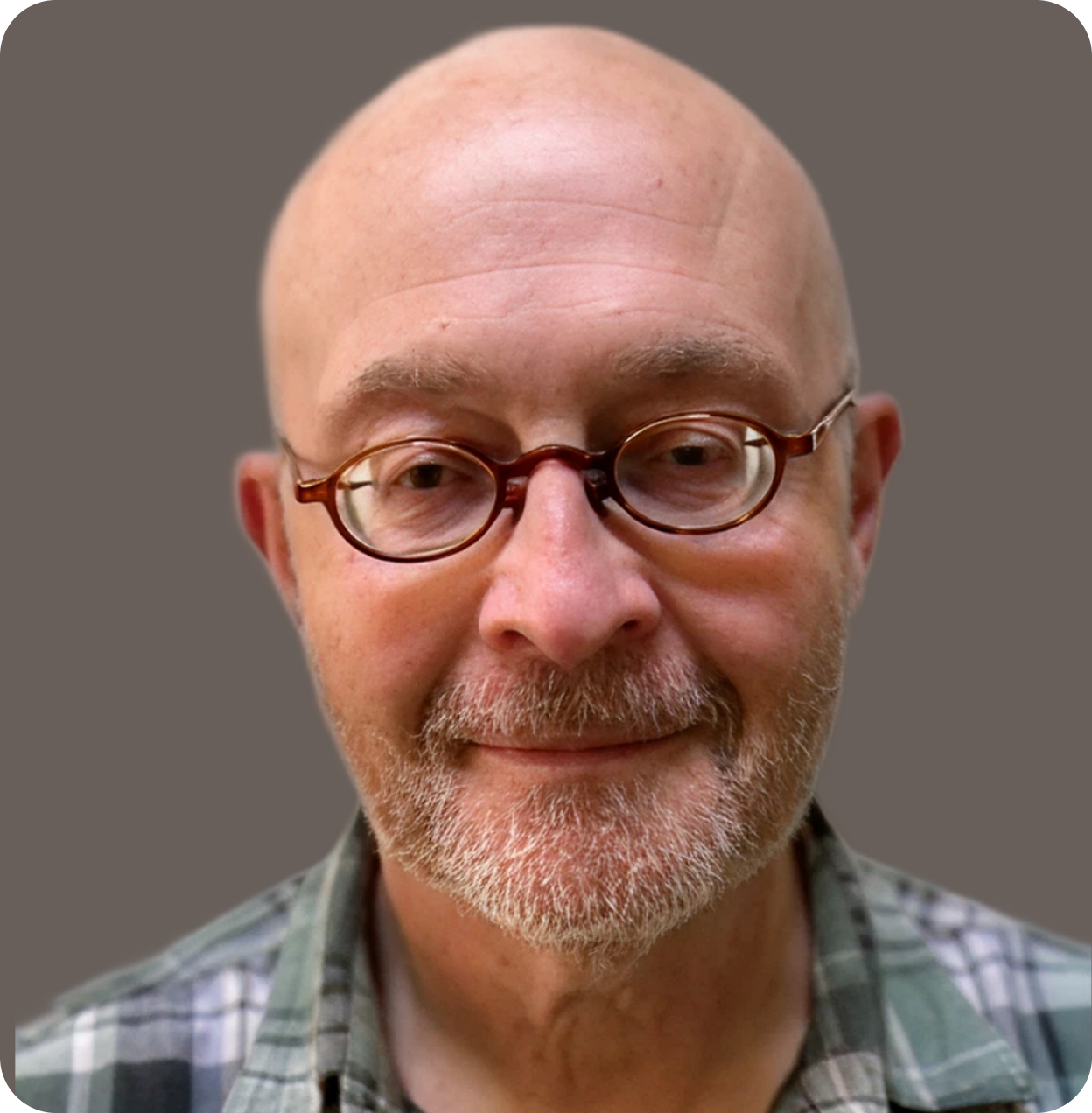Close-up of smiling older man with glasses, beard, and plaid shirt, against a neutral background.