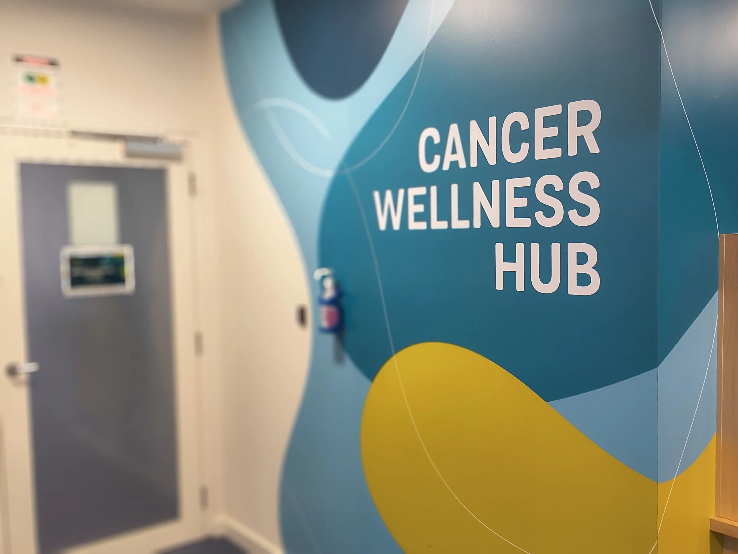 A wall with a blue background displaying the words 'CANCER WELLNESS HUB' in white text