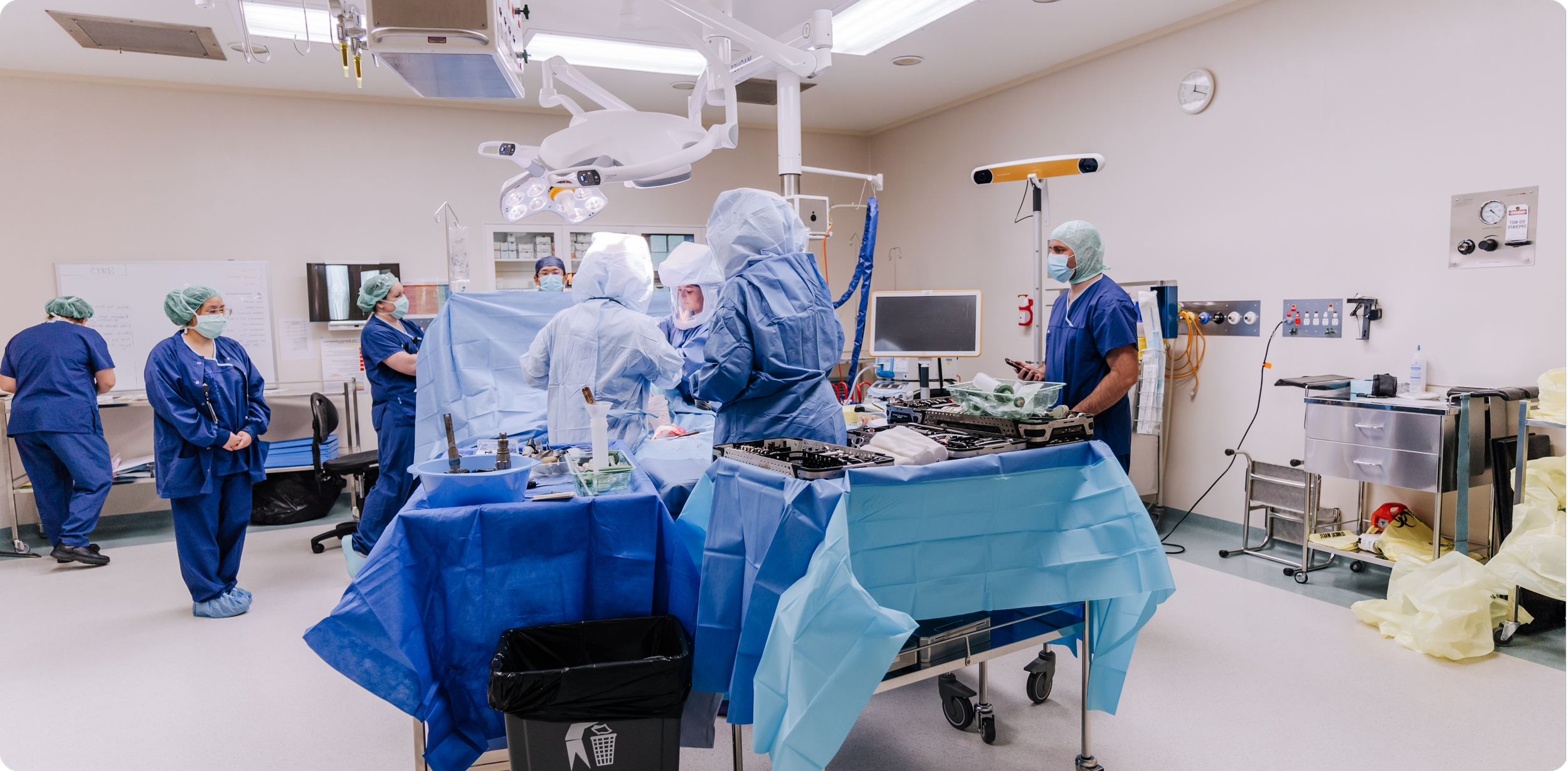 A team of medical professionals performing surgery in an operating room equipped with surgical lights, monitors, and medical equipment.