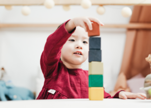 A young child in a red shirt stacking colorful blocks.