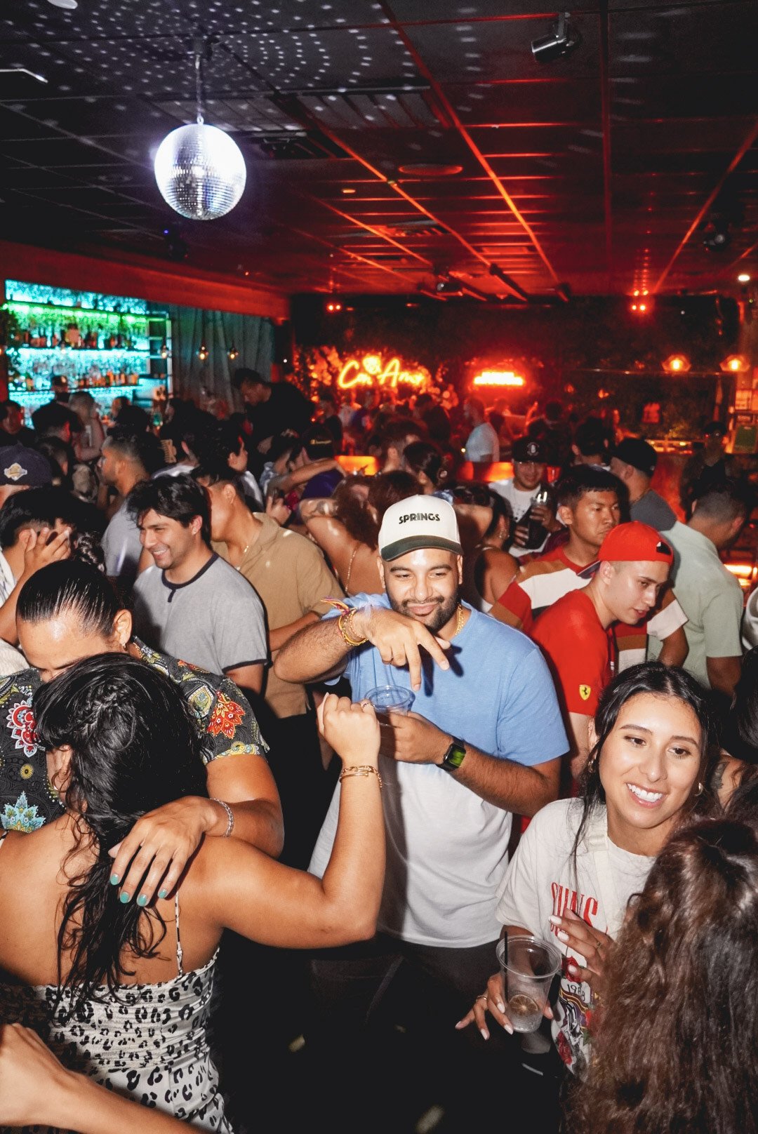 People dancing and socializing in a crowded nightclub with colorful neon signs and a disco ball.