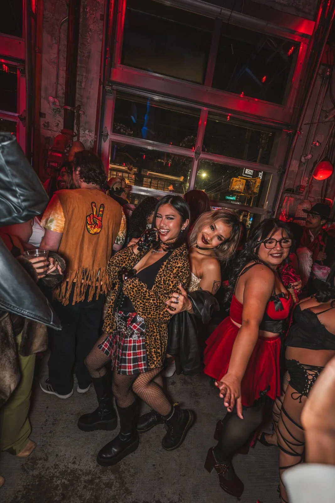 Group in costumes, including a leopard coat and a plaid skirt, dancing by the garage windows at Sea Wolf in Bushwick, Brooklyn