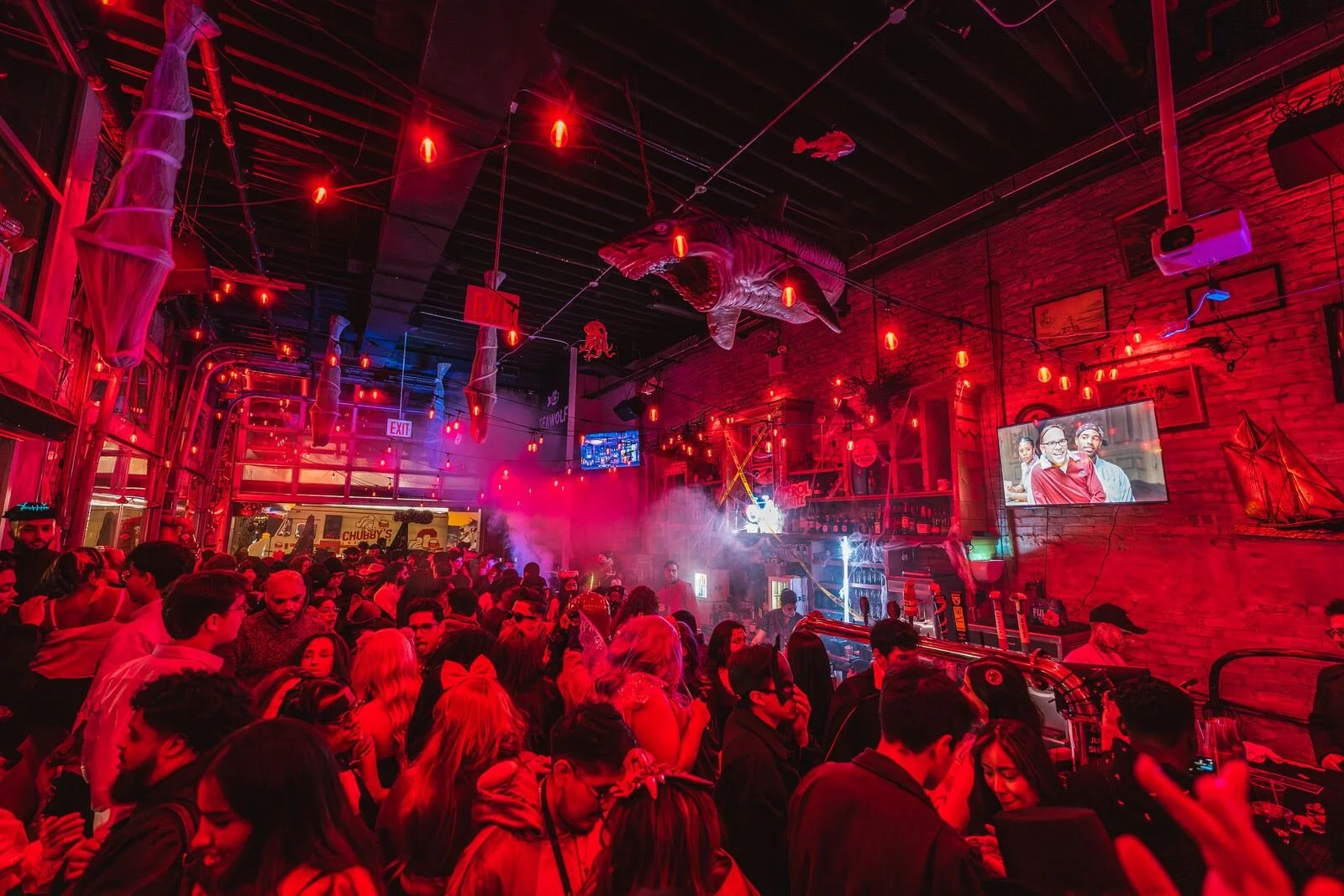 Packed dance floor under red string lights and hanging shark decorations at Sea Wolf in Bushwick, Brooklyn