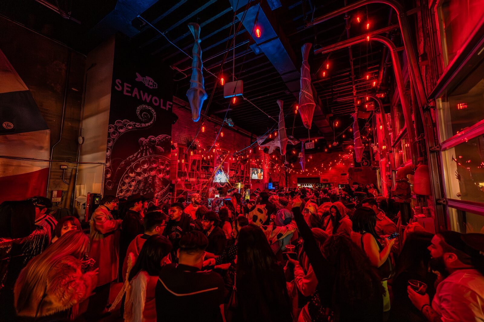 Wide view of a red-lit crowd and shark decorations at a Latin party at Sea Wolf in Bushwick, Brooklyn