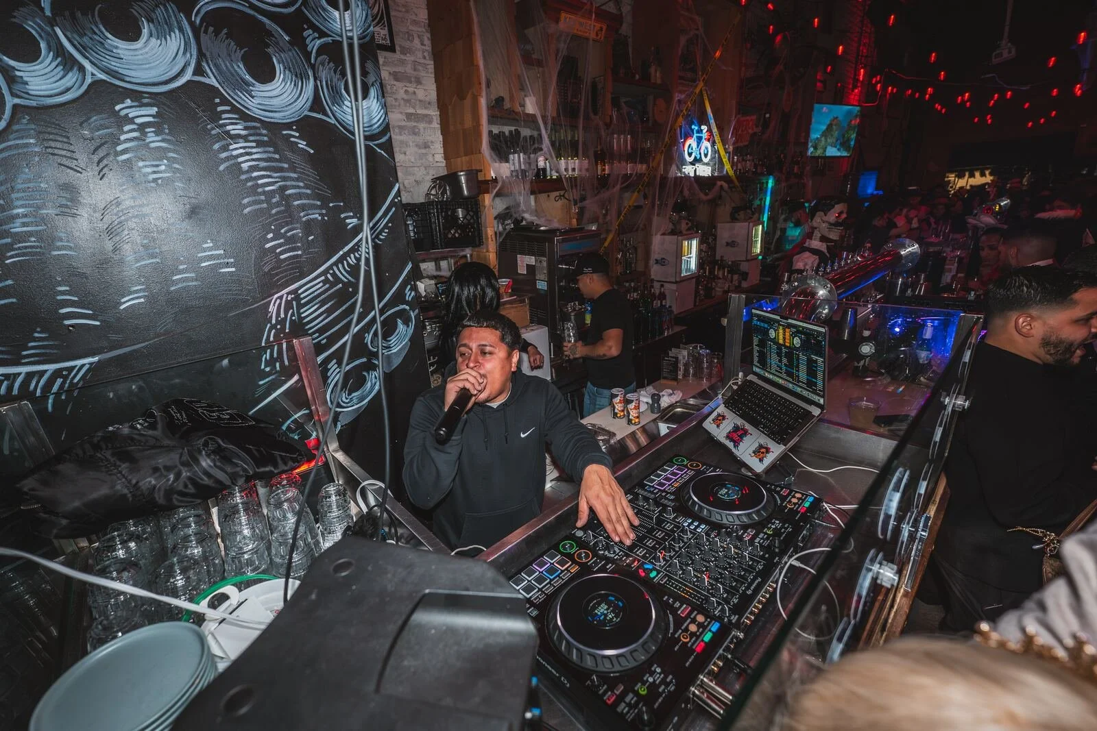 DJ singing into a mic behind the decks, octopus mural behind him, at Sea Wolf in Bushwick, Brooklyn