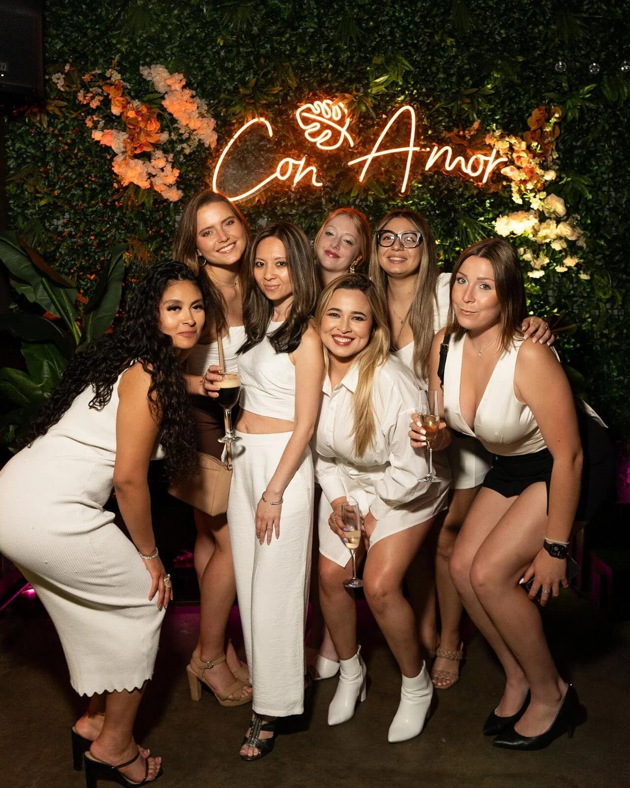 Throwback: friends in white outfits posing under the Con Amor neon sign and flower wall at Republic in Williamsburg, Brooklyn