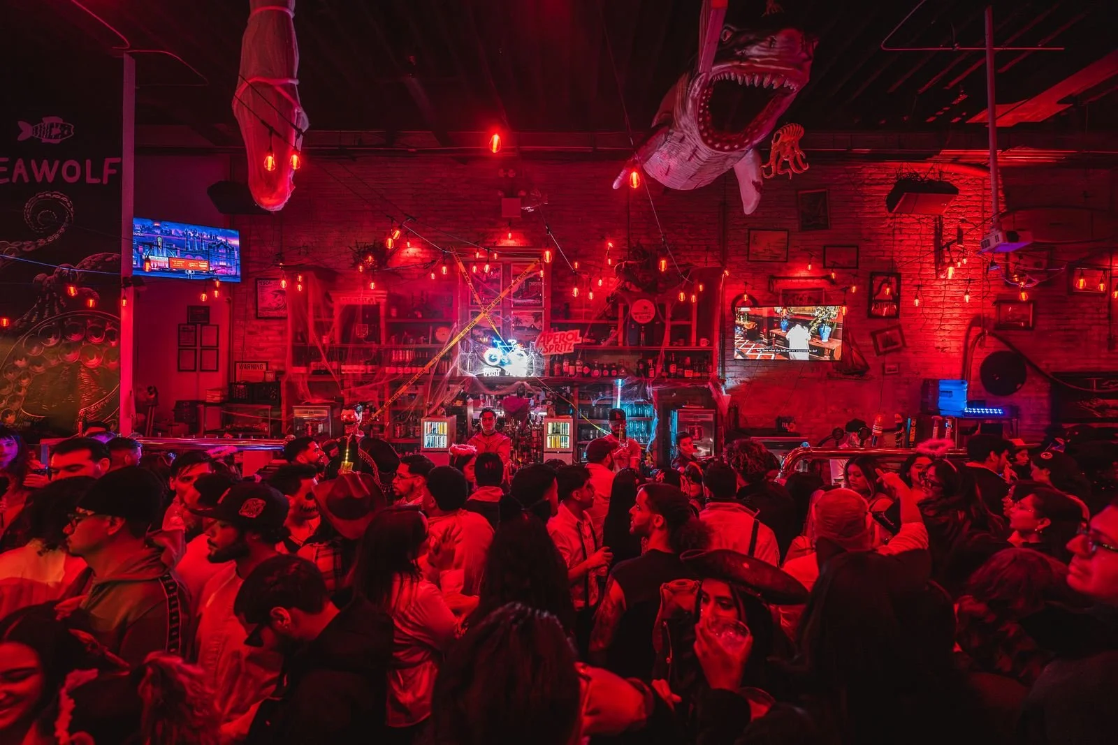 Packed dance floor under red lights and shark decorations at Monstera Nightlife at Sea Wolf in Bushwick, Brooklyn, Halloween 2025
