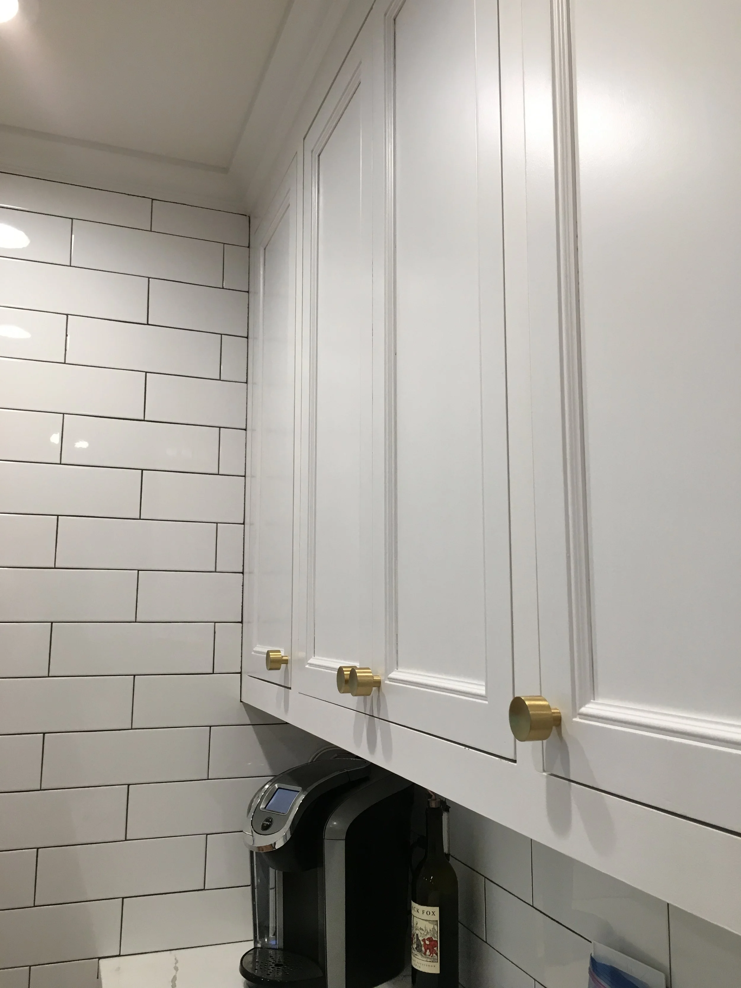Close-up of painted maple cabinets with brass hardware and tile backsplash