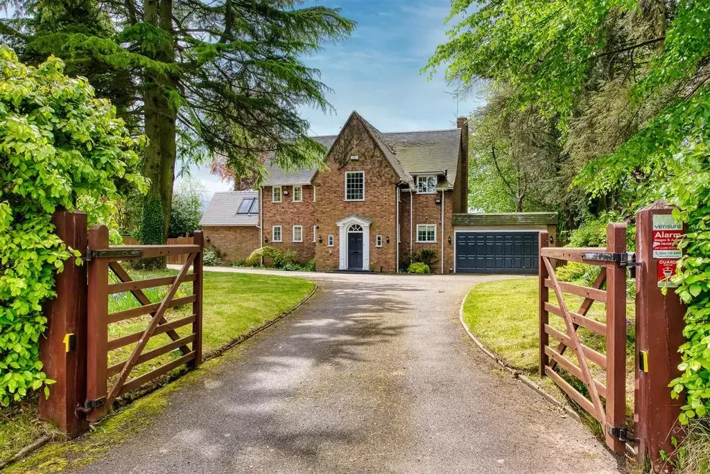 Brick house behind open driveway gate with green lawn and trees.