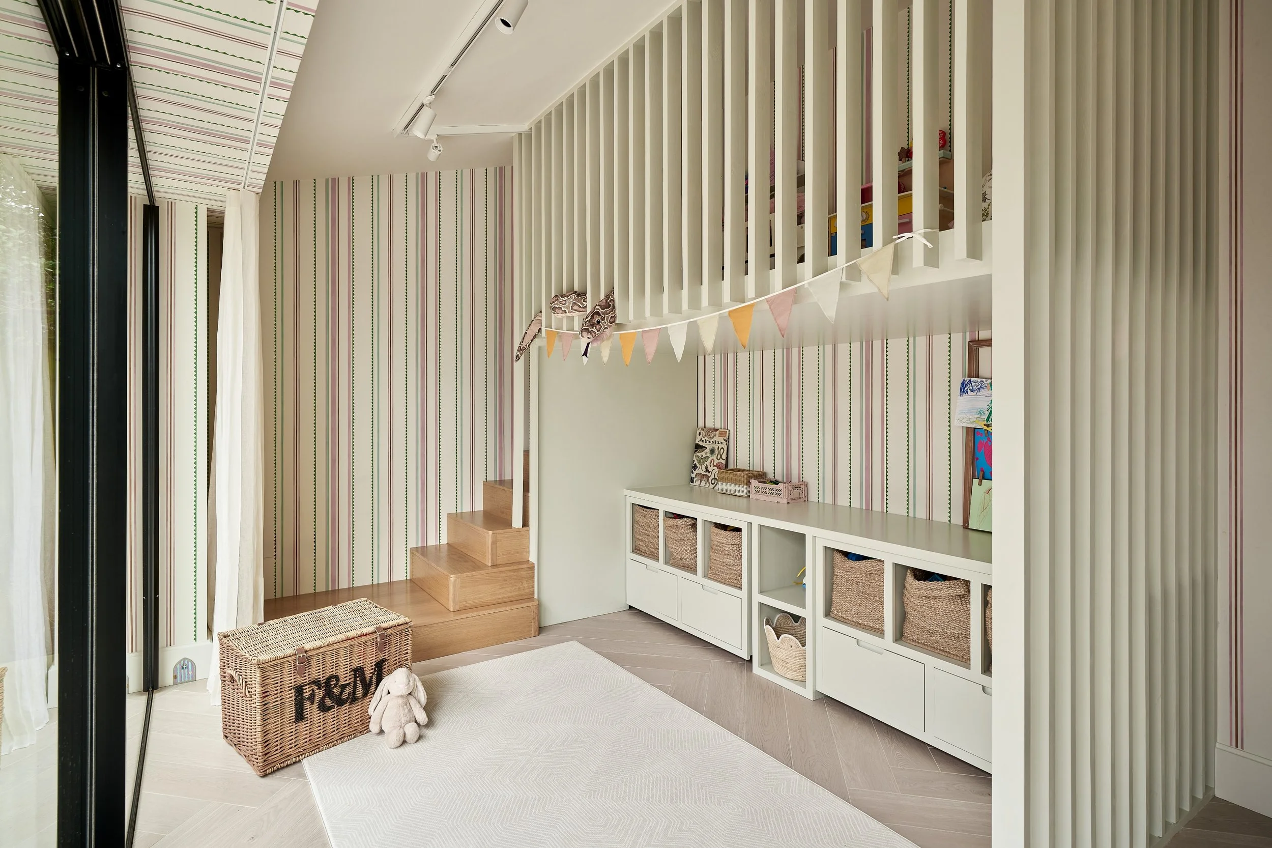 Interior of a room with stairs, striped wallpaper, a white storage unit with baskets, and a fabric bunting hanging from a railing.