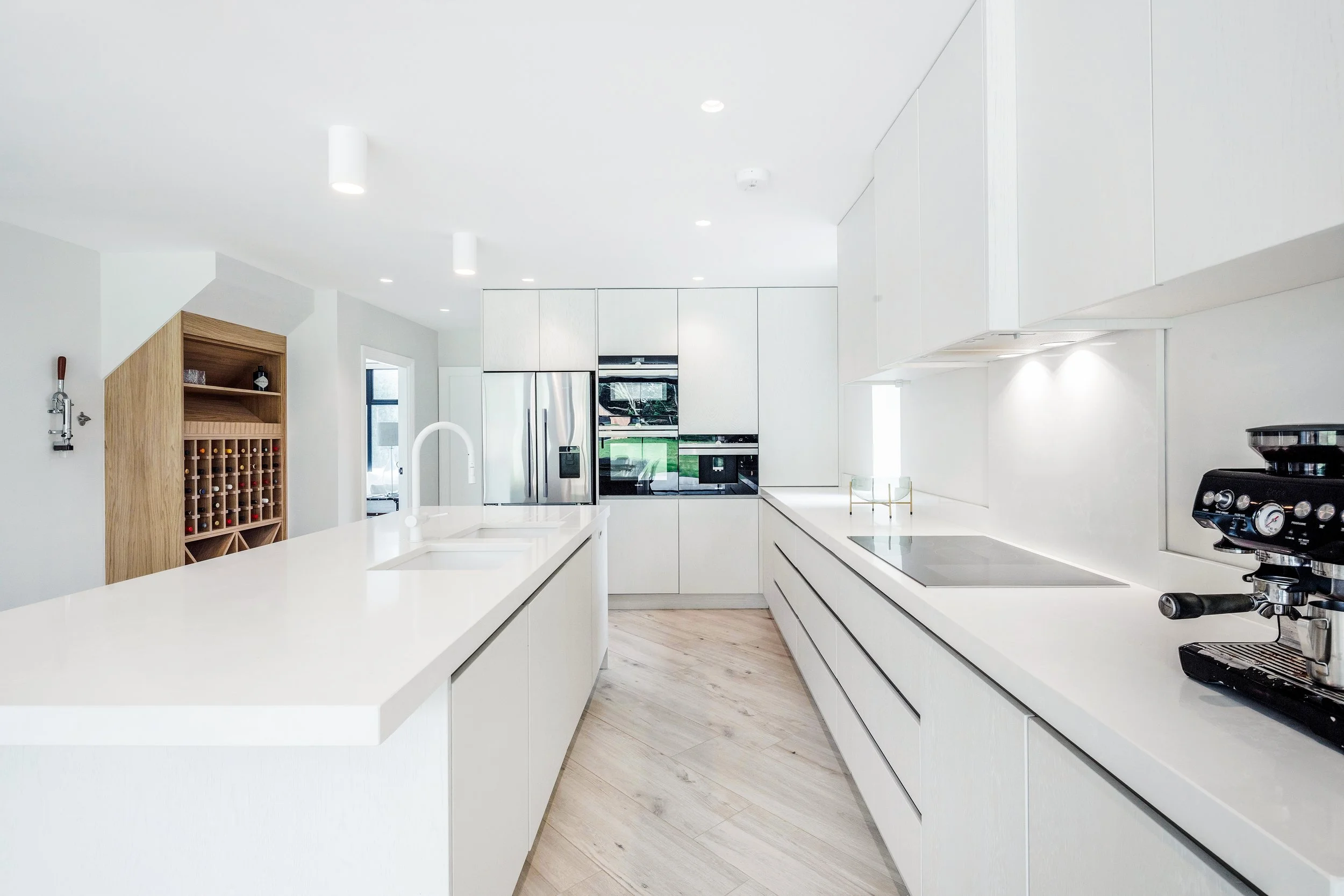 Modern white kitchen with island, built-in appliances, and light wood flooring.