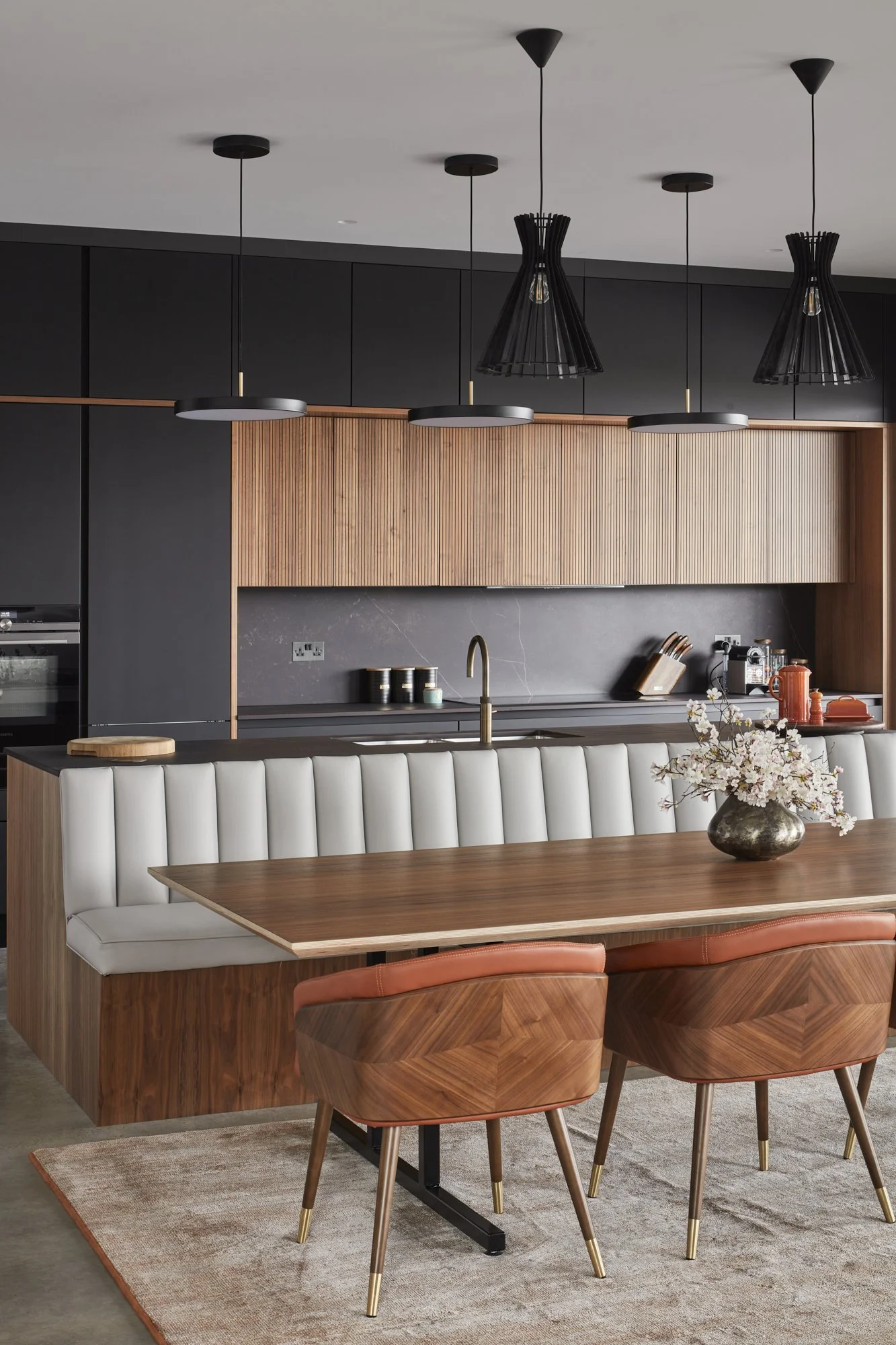 Modern kitchen with black and wooden cabinets, a dining table with white and brown chairs, and a centerpiece of flowers in a vase.