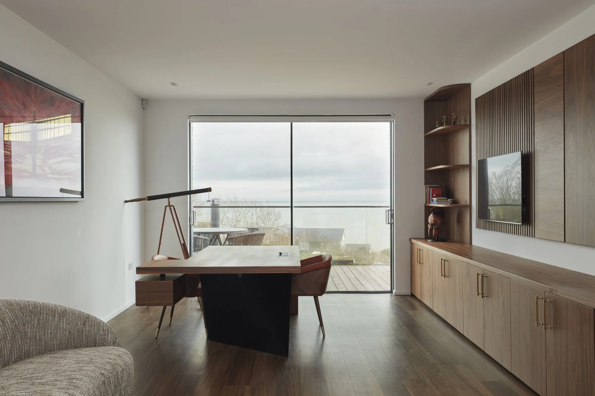 Modern living room with wooden cabinets, a wall-mounted television, a bookshelf with decorative items, a telescope by the window, and a sliding glass door leading to a balcony.