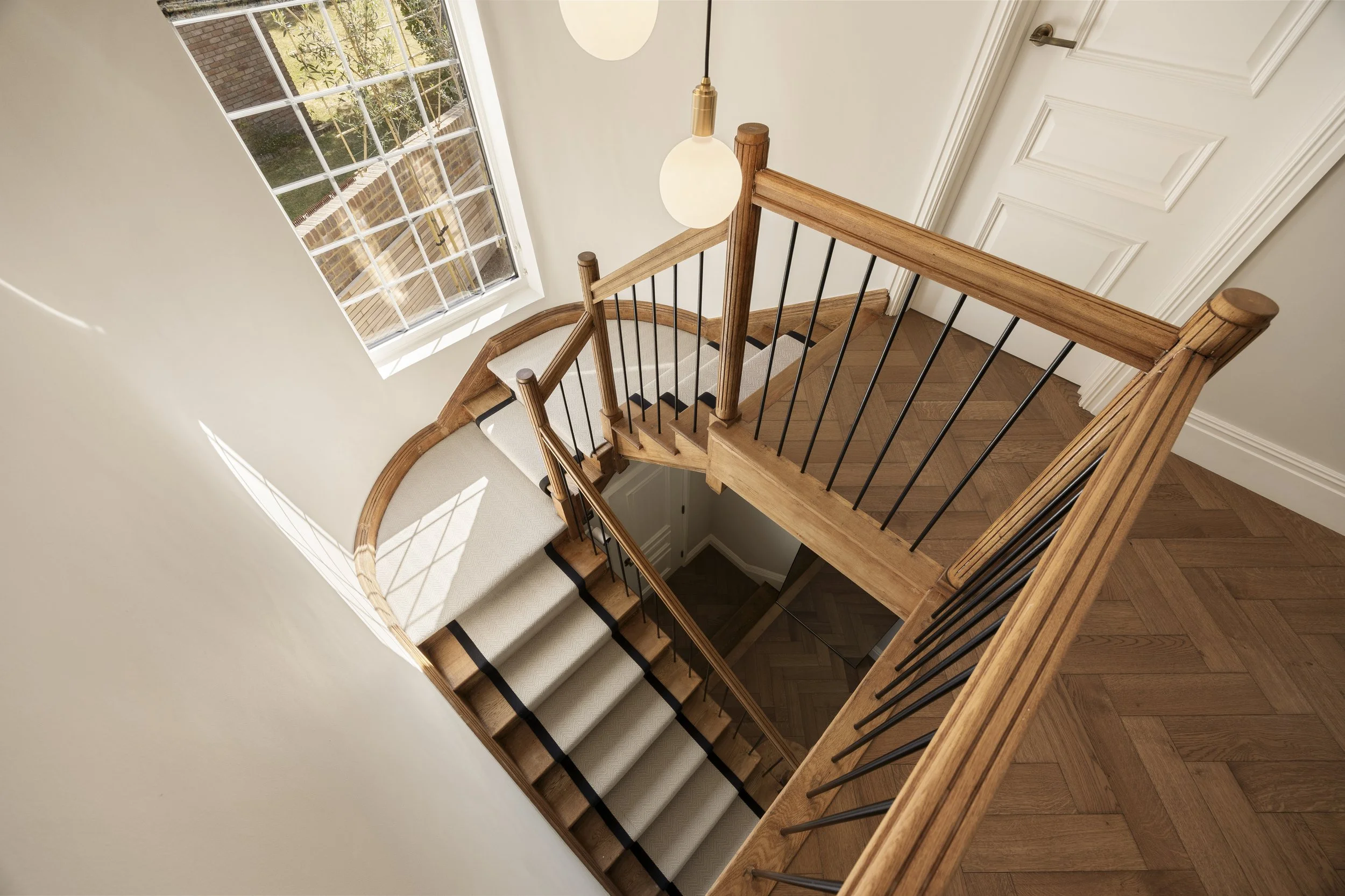 View of a staircase with wooden handrails and black vertical balusters inside a home, illuminated by natural light from a large window.