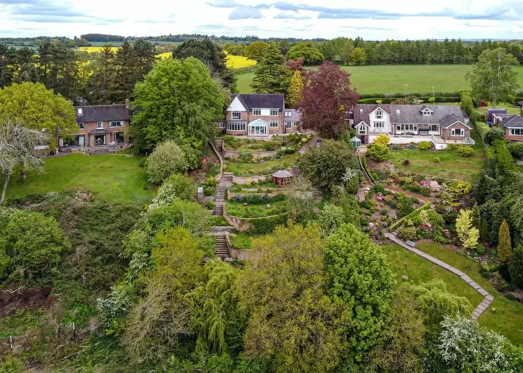 Aerial view of a residential neighborhood with large houses, lush trees, and landscaped gardens, segmented by terraced steps and pathways.