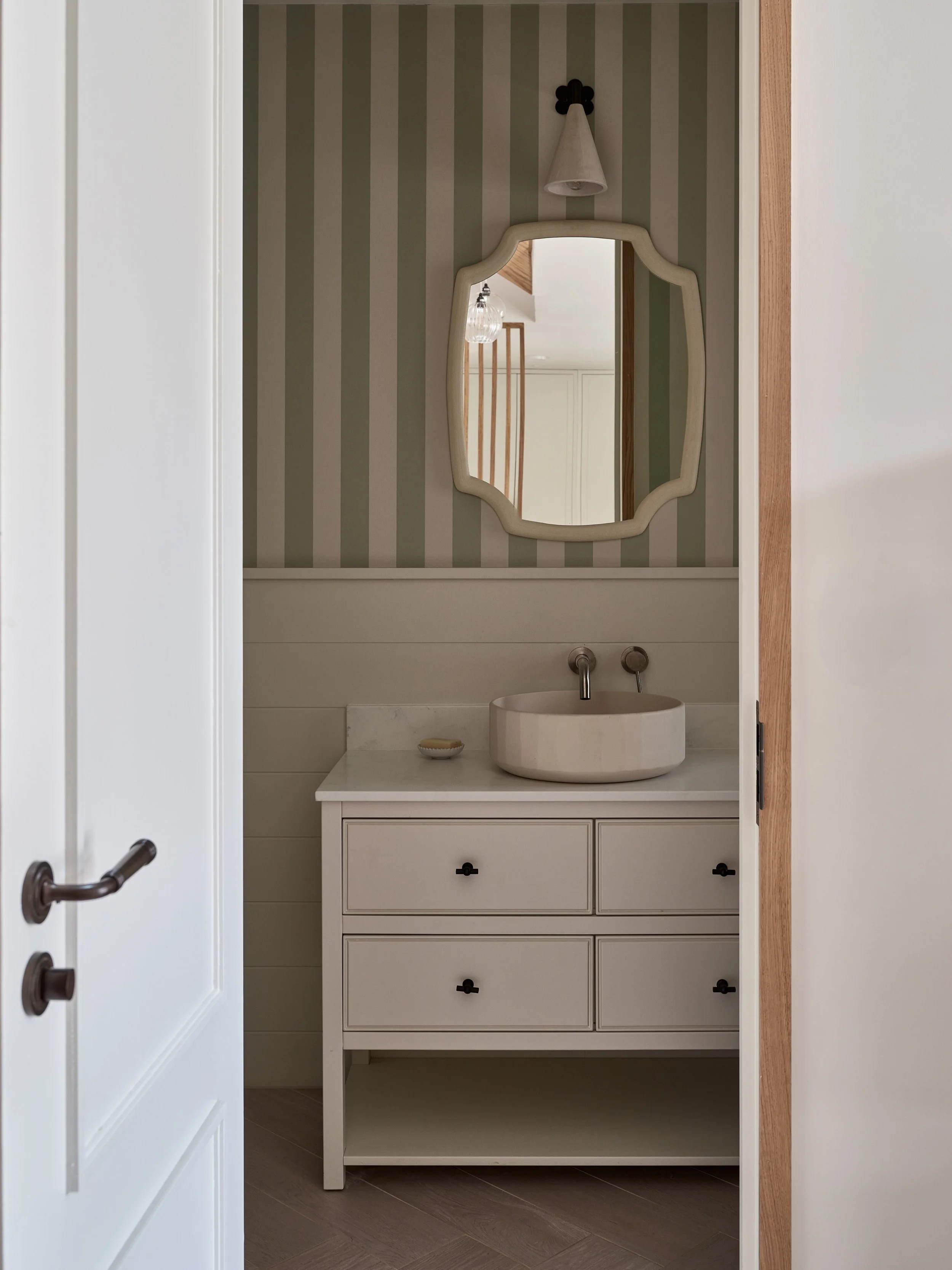 Bathroom vanity with a round vessel sink, a mirror, wall-mounted faucet, a small soap dish, and a cabinet with three drawers.