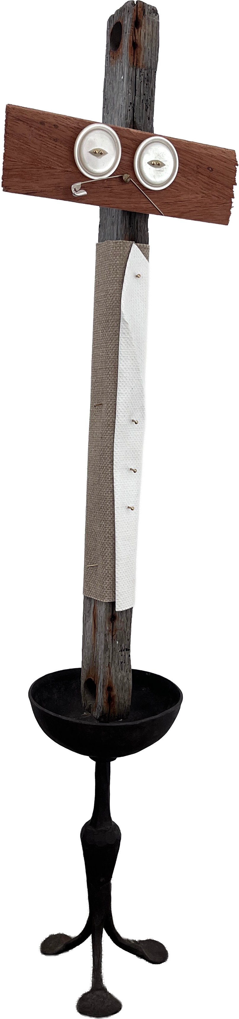 A mixed-media sculpture of a face with two white buttons for eyes, mounted on a weathered wooden post with additional wood and fabric elements, resembling a whimsical or abstract face.