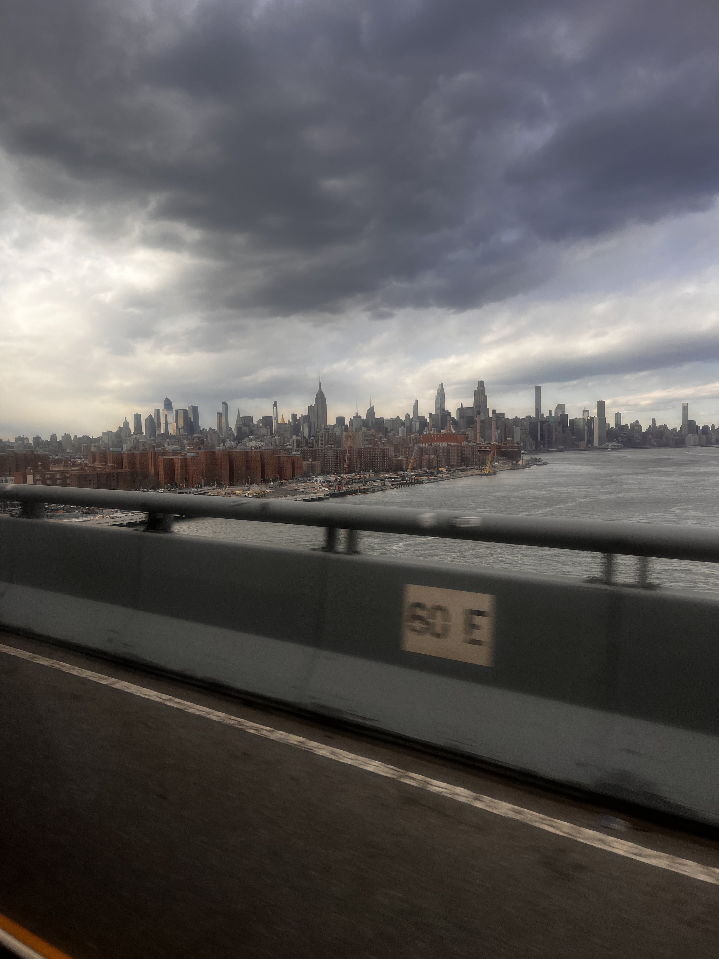 New York skyline seen from a moving vehicle with dark, cloudy skies overhead.