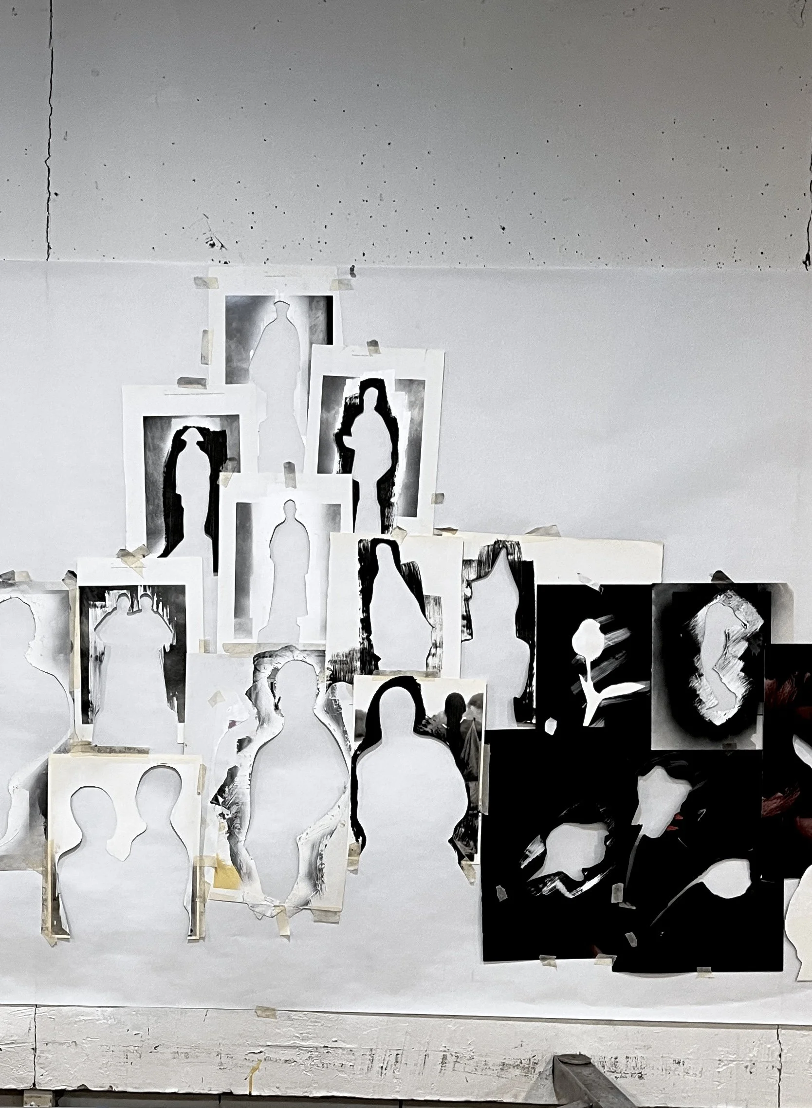 A series of stencil portraits in black and white on paper, taped to a wall, depicting various silhouettes of people, arranged in a loose collage style.
