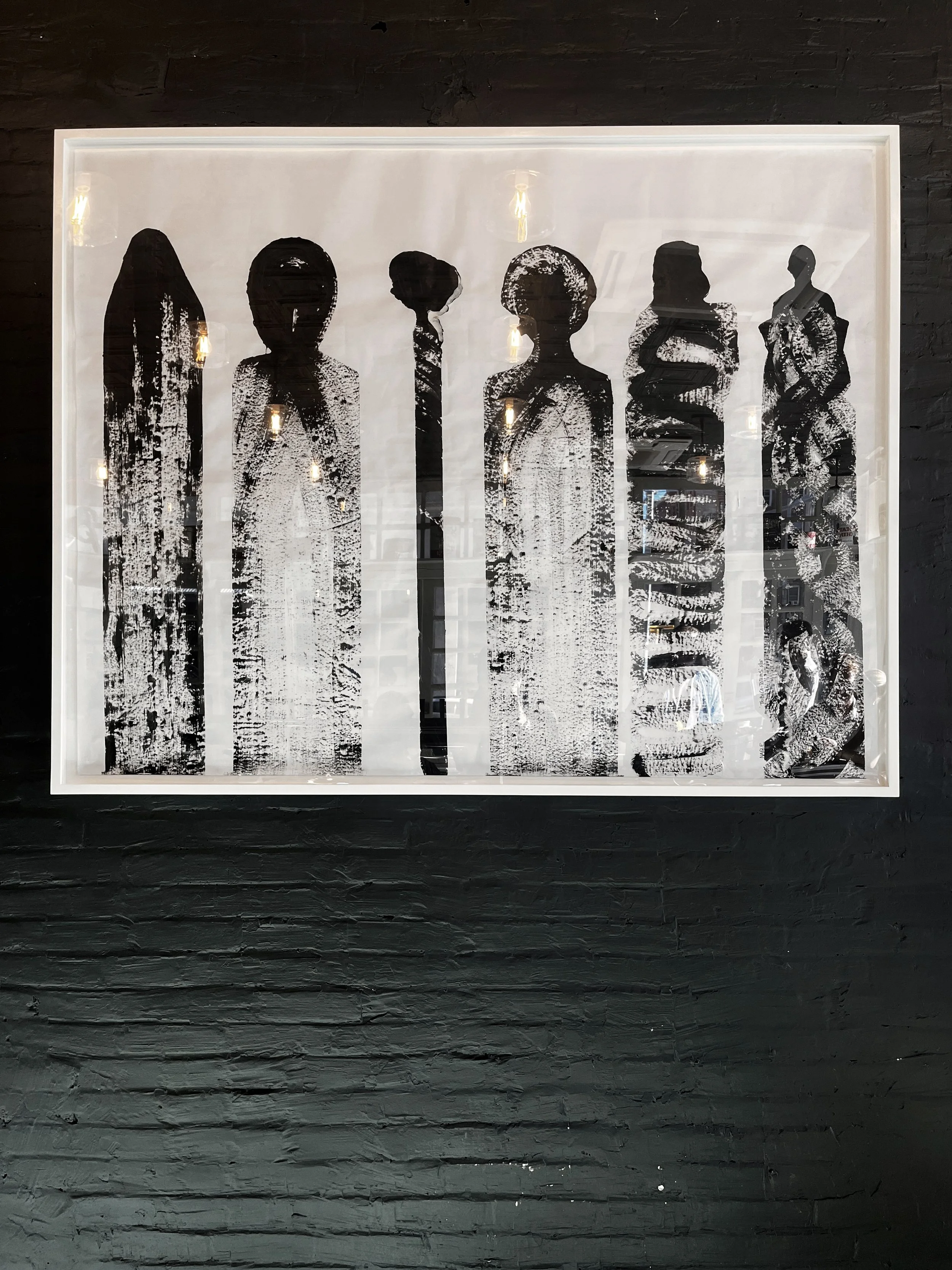 Black and white artwork featuring six human silhouettes with textured patterns, framed on a black brick wall.