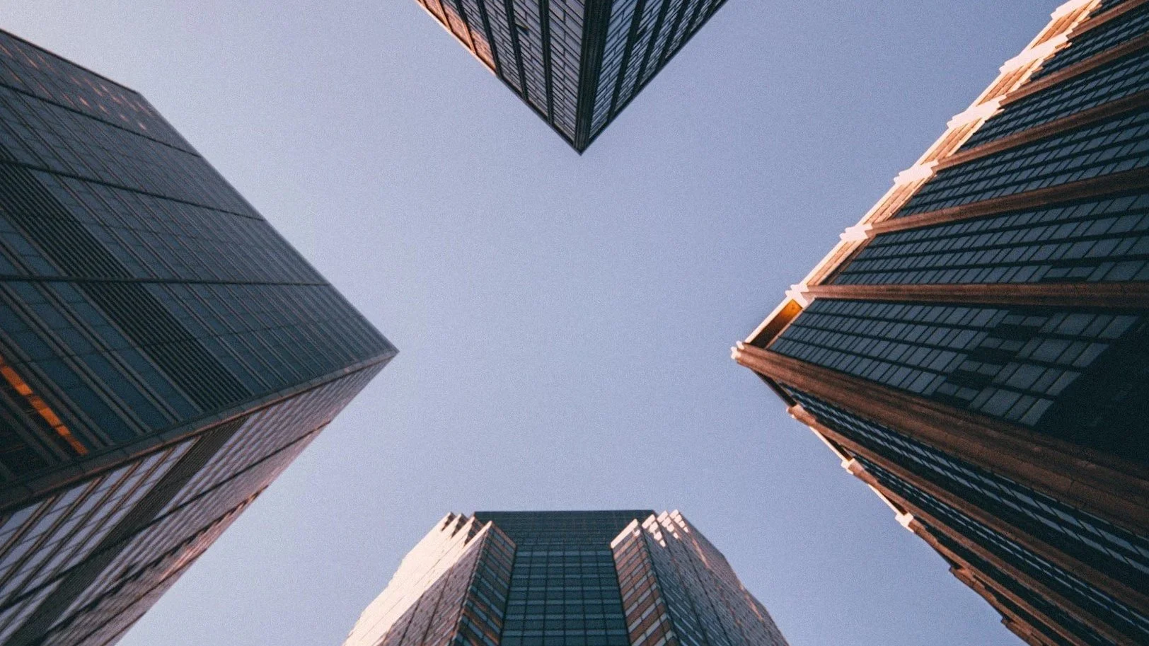 Looking up at tall modern skyscrapers with reflective glass windows against a clear sky.
