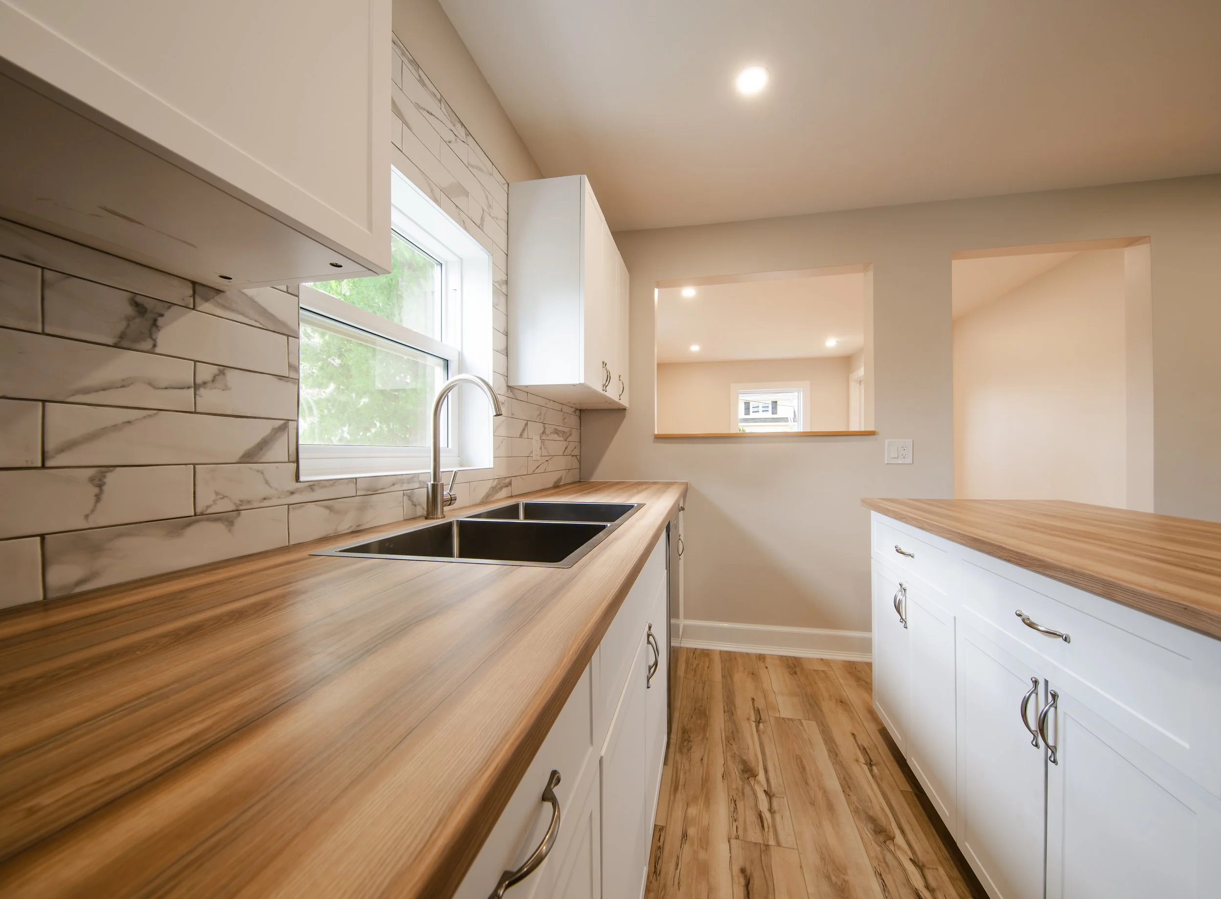 freshly remodeled kitchen with wooden countertops, white cabinets, a window, a modern sink, beige walls, and hardwood floors.
