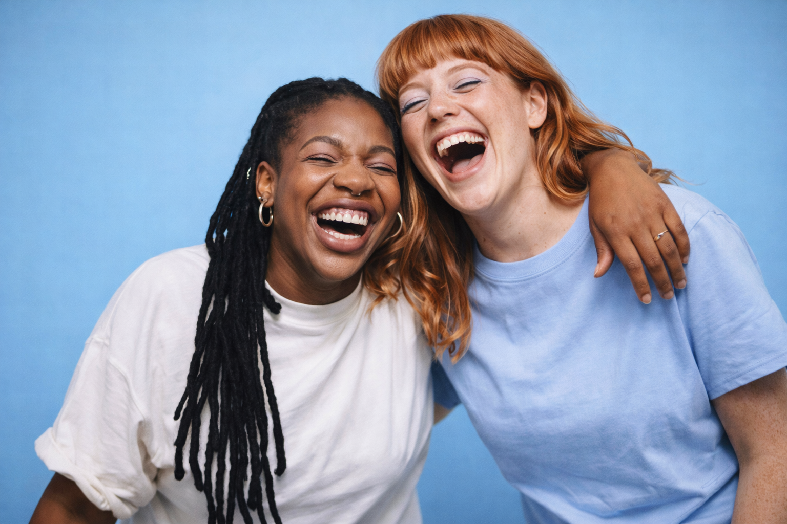 Two women laughing and hugging each other against a blue background.