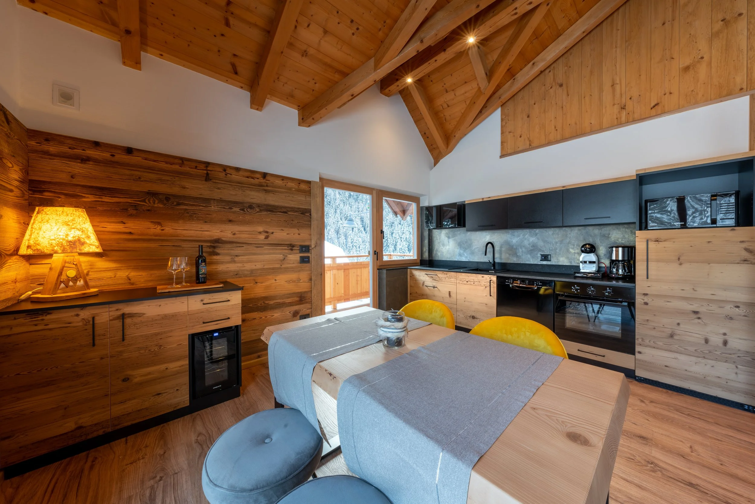 Interno di una cucina in legno con tavolo apparecchiato, sedie gialle e un'illuminazione calda.