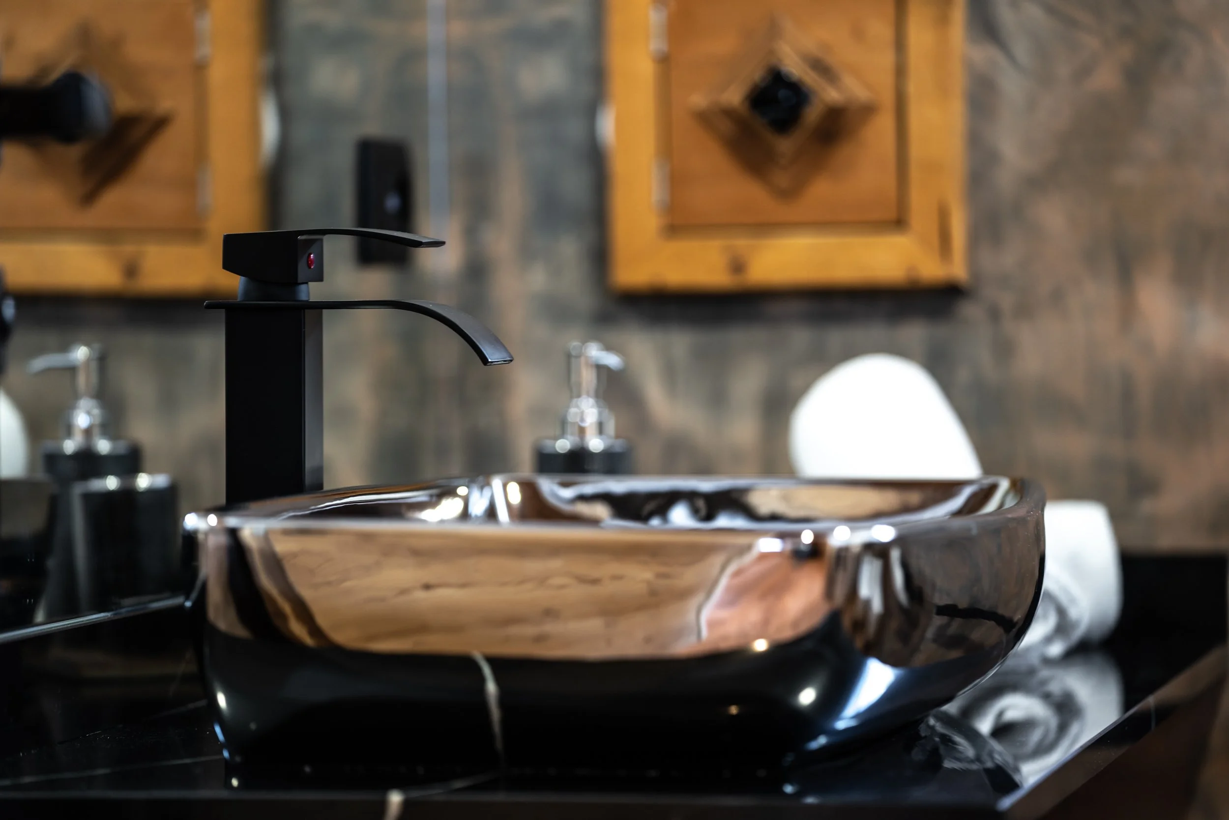 Lavabo di design in ceramica con rubinetto nero su superficie nera, sfondo con pareti in legno e accessori da bagno.