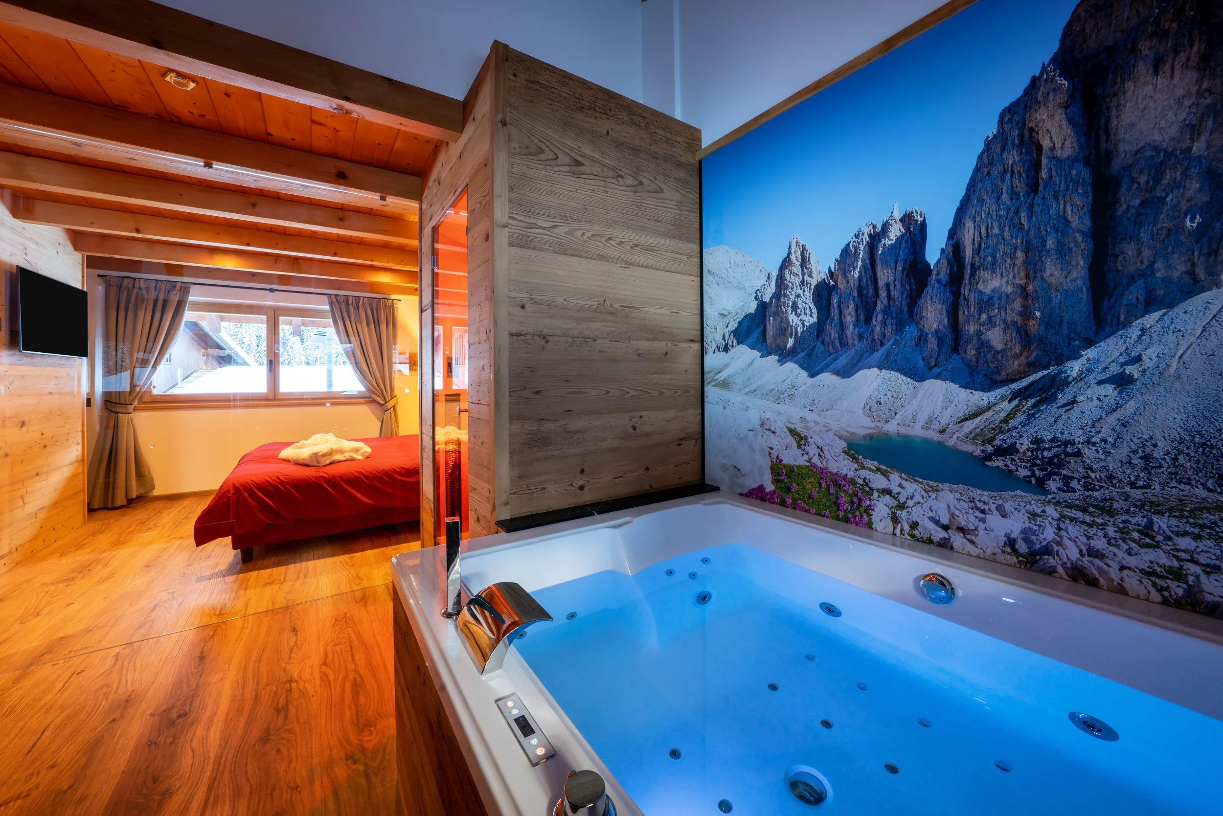 Camera da letto con finestra vista su neve e alberi, bagno con jacuzzi e grande parete decorata con paesaggio montano