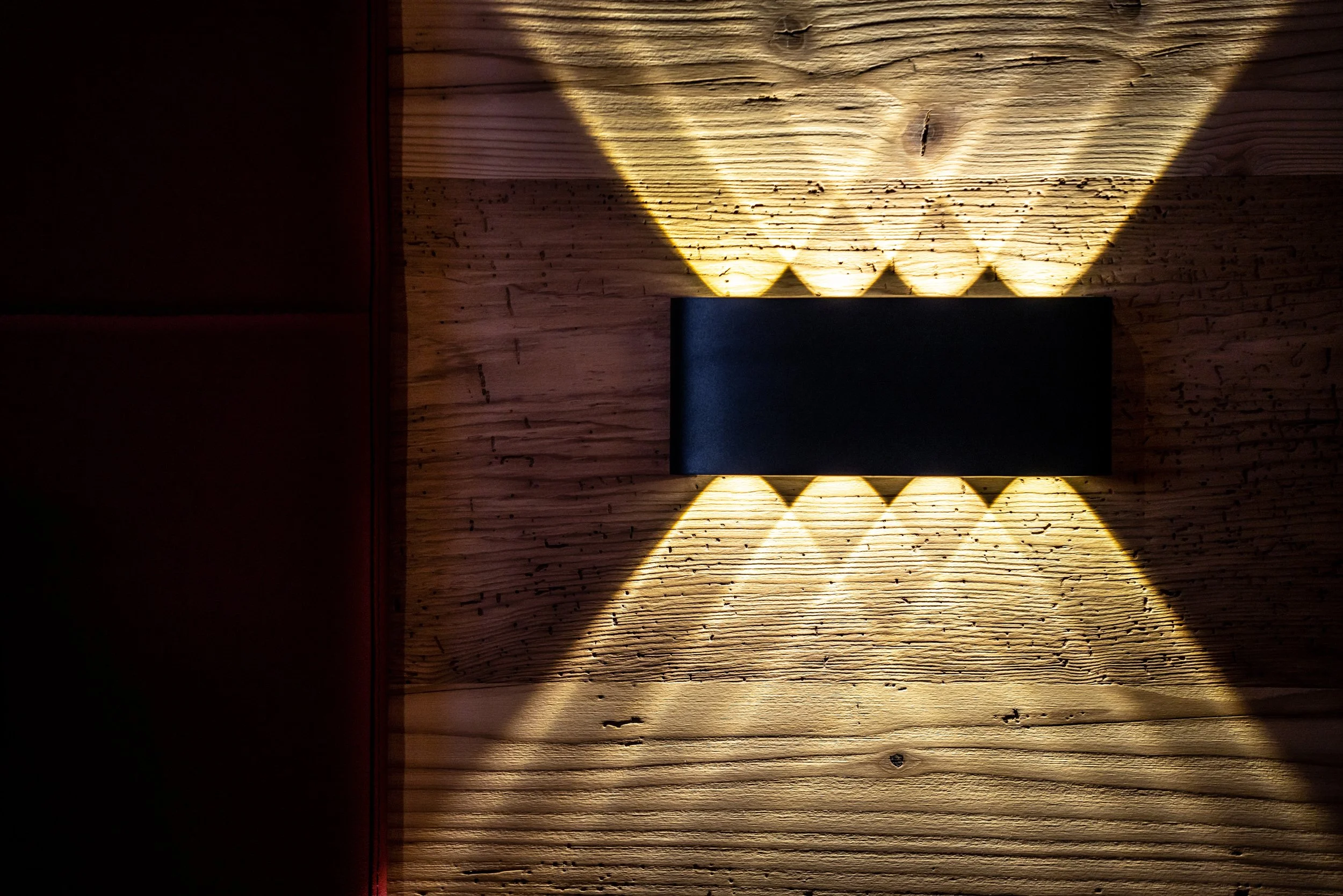 Lampada da parete con luce calda che crea motivi geometrici sulla parete di legno