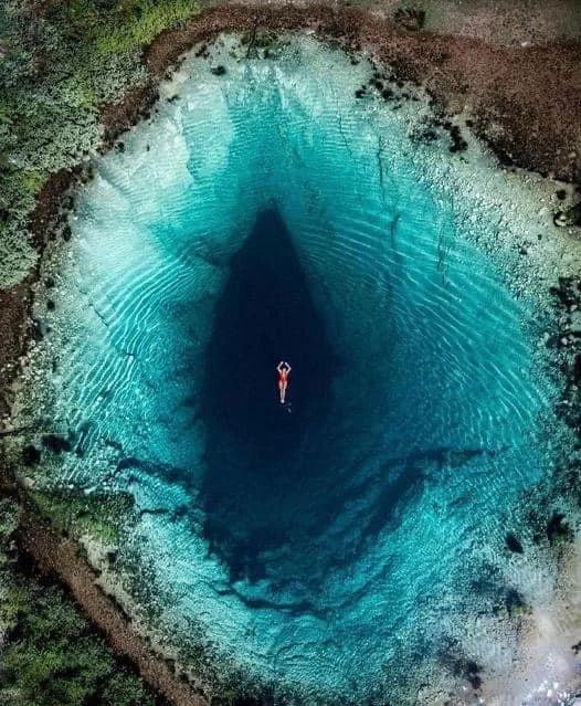 Vrouw die zich ontspannen laat drijven in een ovaalvormig helderblauw meer, gevormd in een natuurlijke krater.