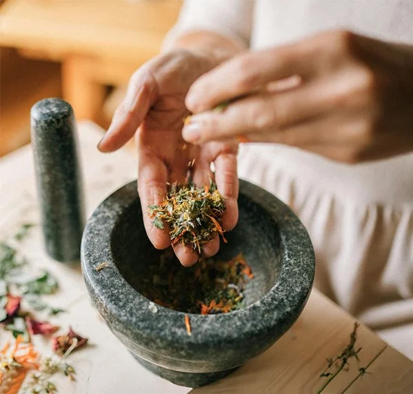 Handen die kruiden fijnmaken tijdens een ambachtelijk selfcare-ritueel in de natuur.