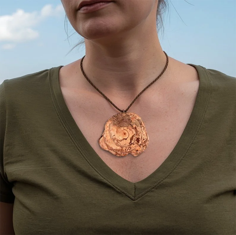 Persoon draagt een groene V-hals T-shirt en een grote houten schelprandketting.