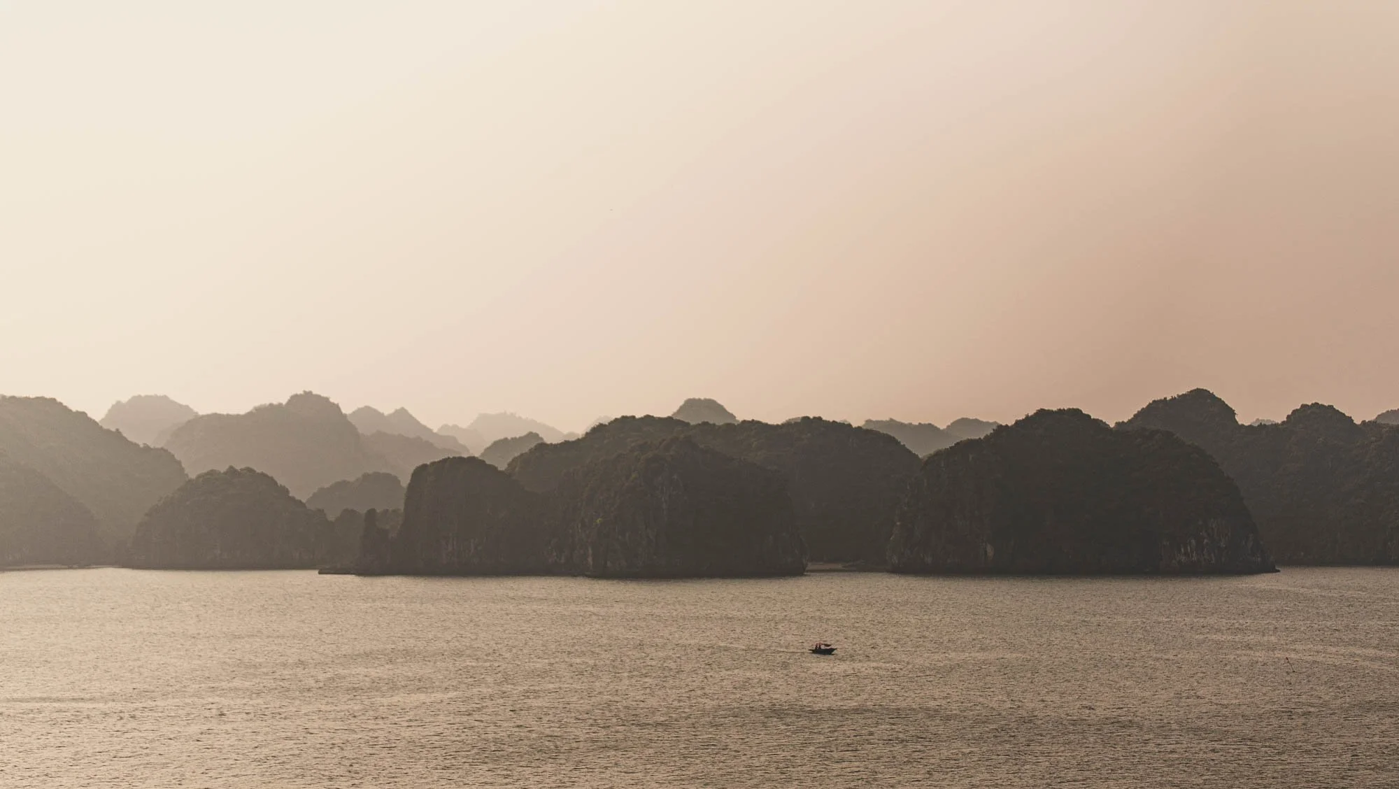 A body of water with dark green, rocky islands in the background, and a small boat on the water.