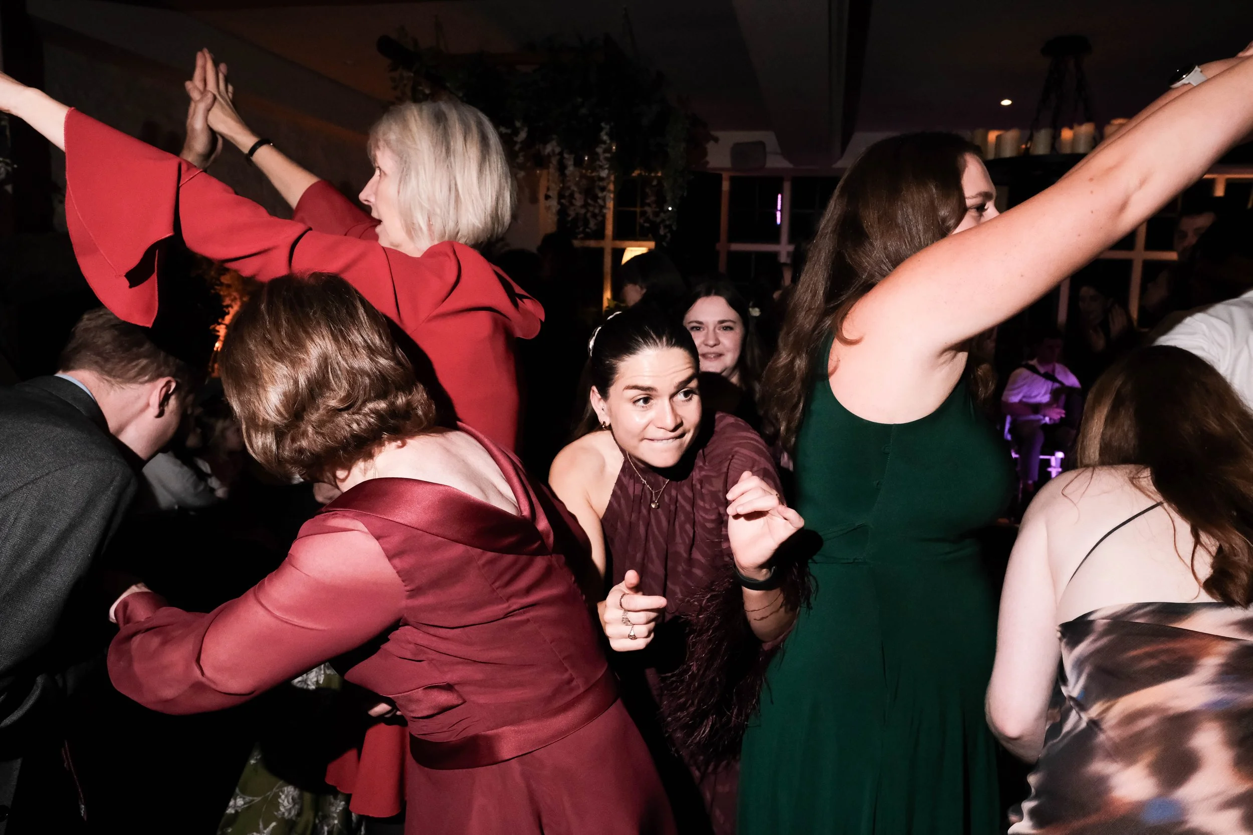 People dancing in a crowded party or event, some with hands raised and others close together in a lively atmosphere.