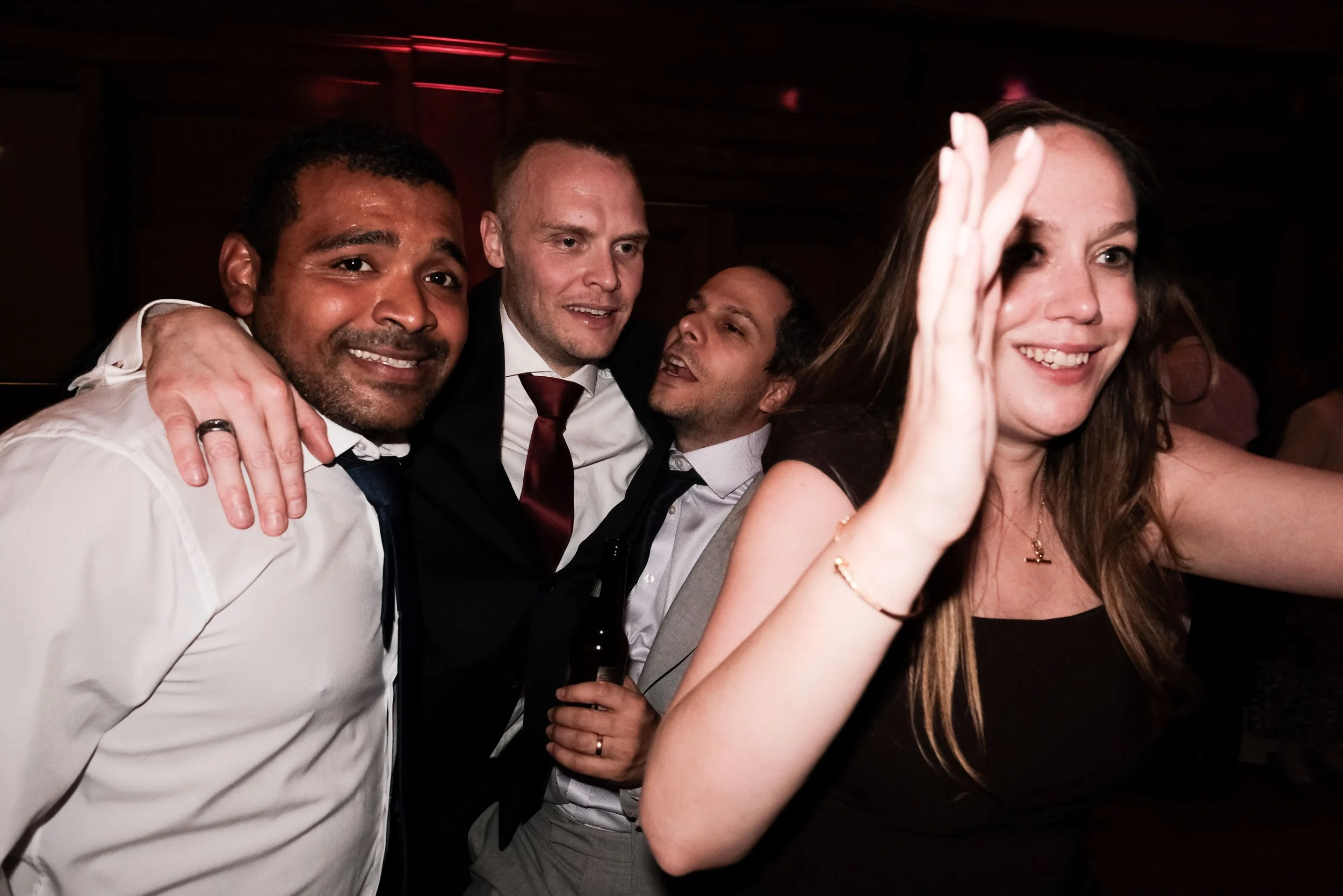 Group of four people at a party taking a selfie, smiling, with a woman on the right holding the phone