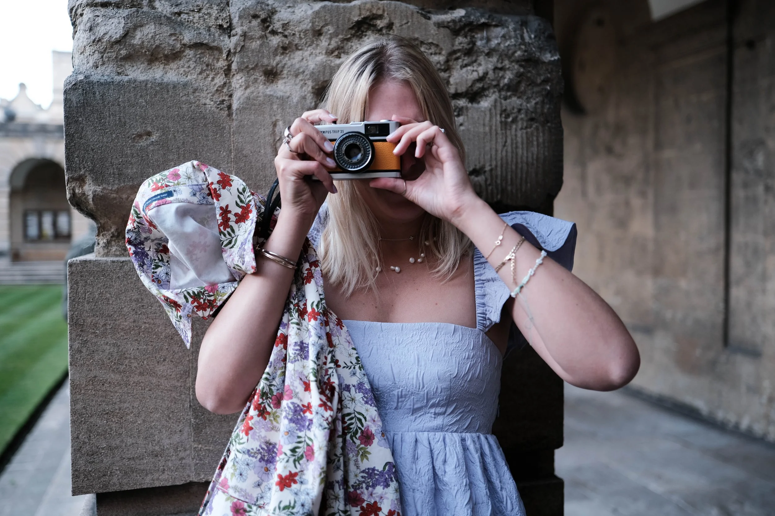 A woman taking a photo with a vintage camera outdoors near a stone wall.