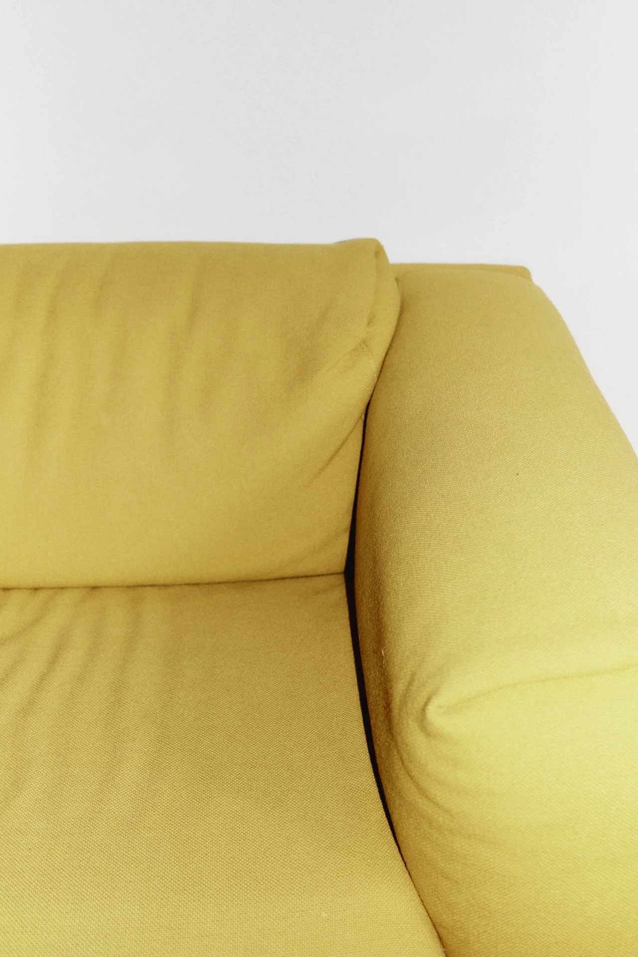 Close-up of a yellow sofa with beige cushions against a white wall.