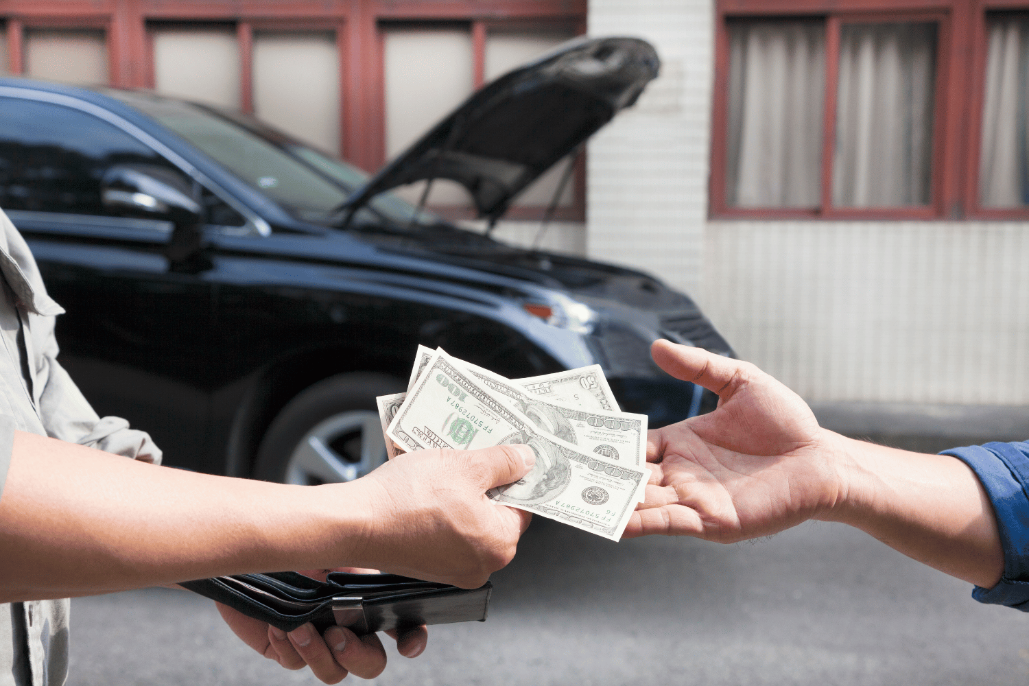 Person handing over cash to another person outside a car with its hood open.