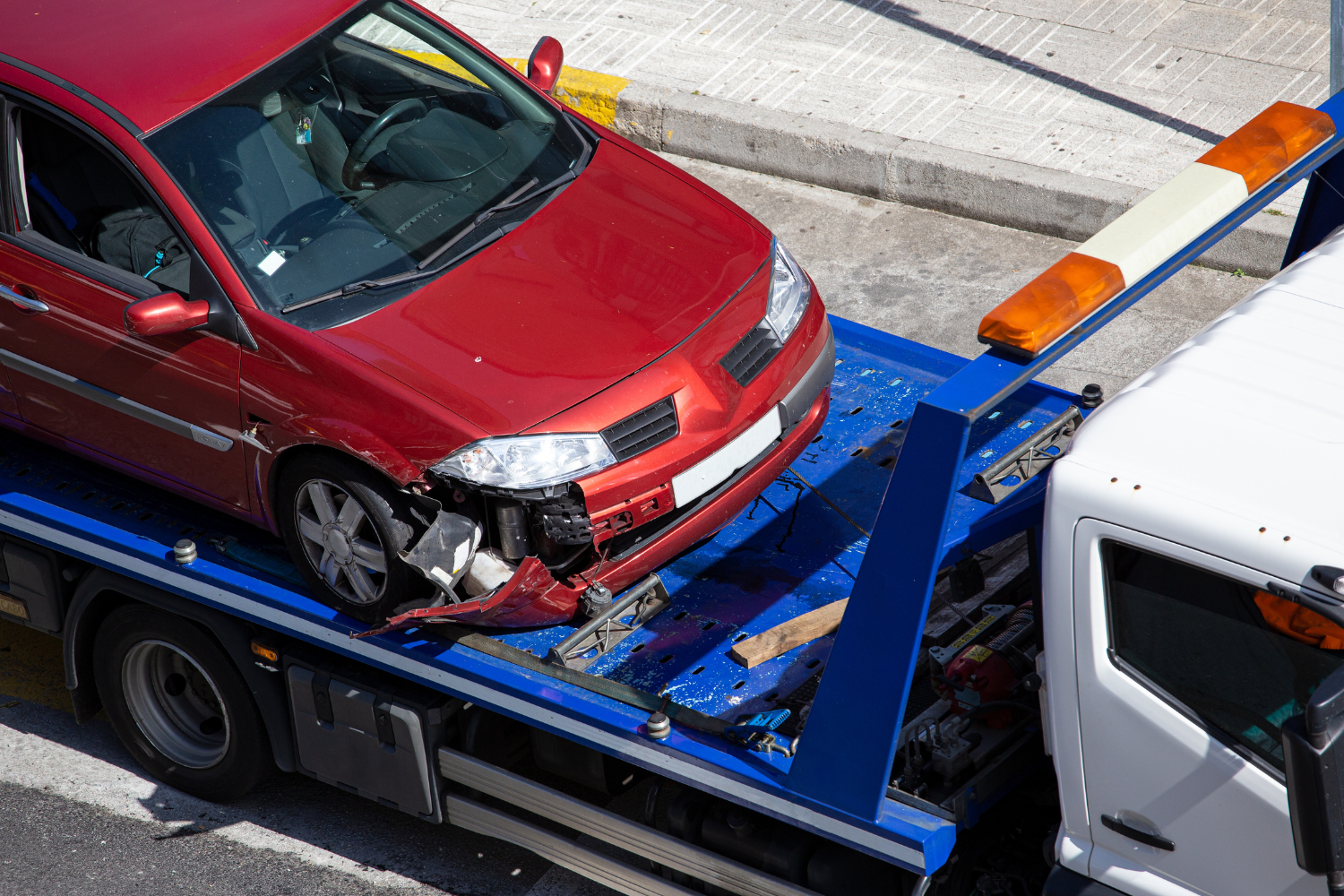 Red car with front damage being loaded onto a flatbed tow truck.