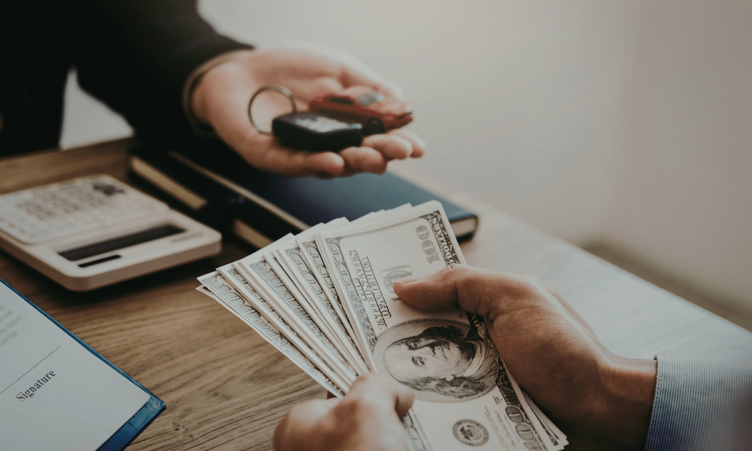 Person handing over a stack of hundred-dollar bills to another person at an office desk.